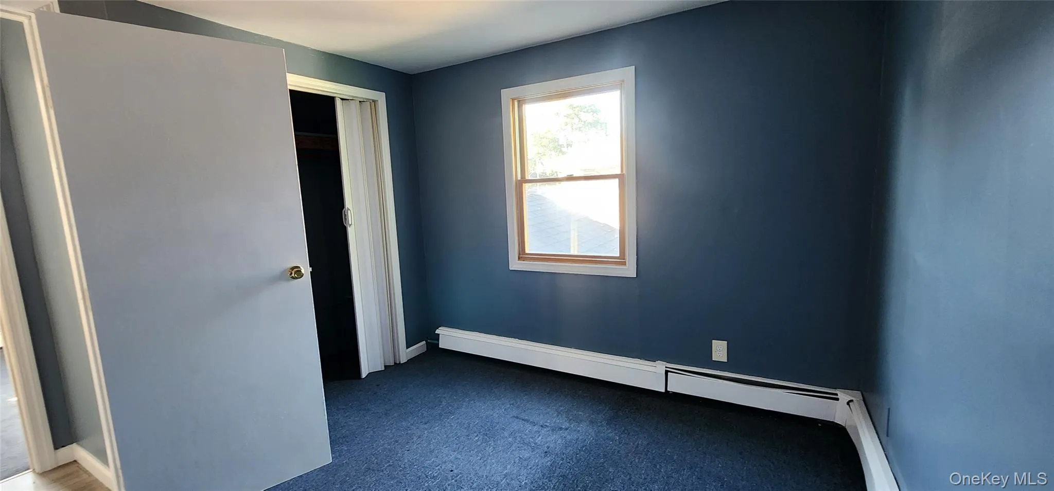 Unfurnished bedroom with a baseboard radiator and dark carpet Unfurnished bedroom with a baseboard radiator and dark carpet