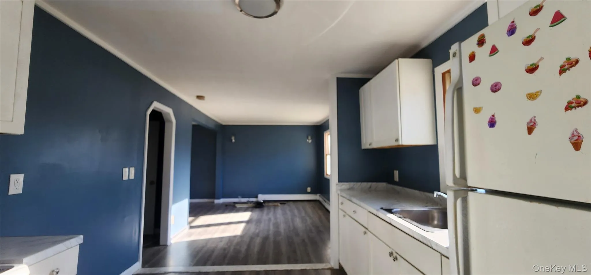 Kitchen featuring freestanding refrigerator, white cabinetry, light countertops, arched walkways, and dark wood-style flooring Kitchen featuring freestanding refrigerator, white cabinetry, light countertops, arched walkways, and dark wood-style flooring