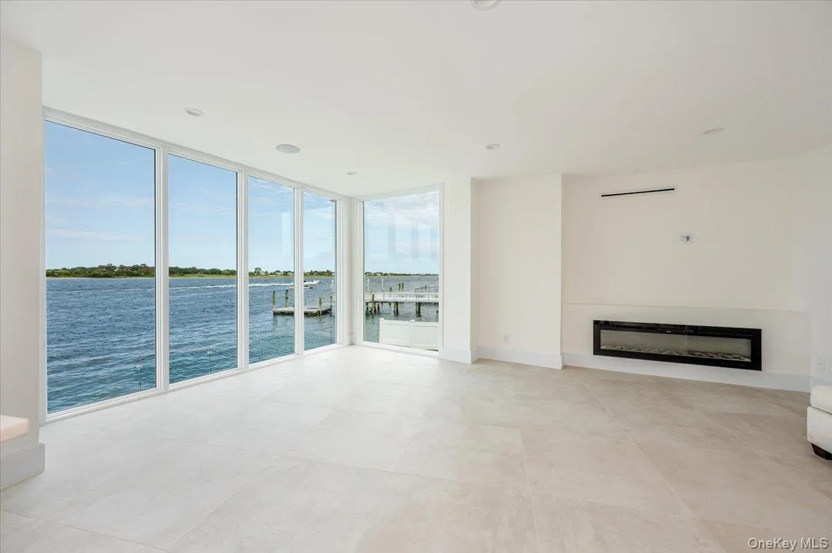 Unfurnished living room with floor to ceiling windows, a glass covered fireplace, a water view, and recessed lighting Unfurnished living room with floor to ceiling windows, a glass covered fireplace, a water view, and recessed lighting