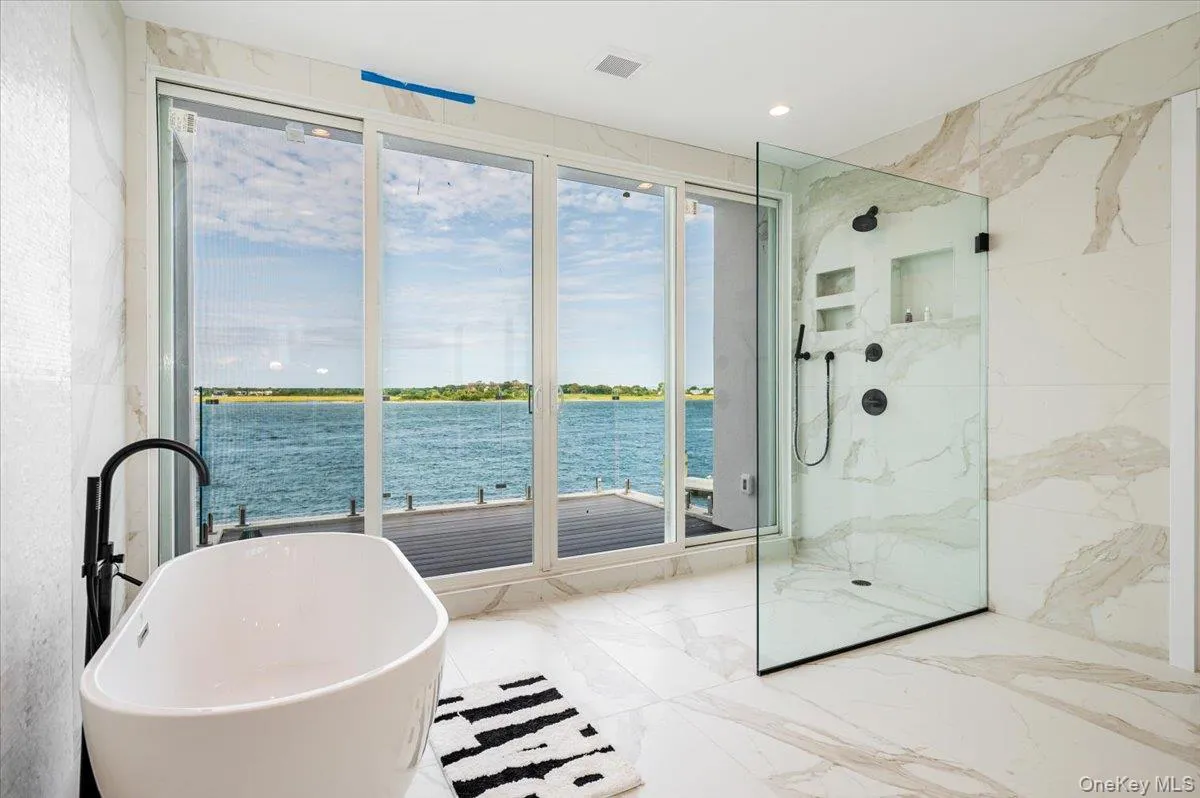 Bathroom featuring marble tiled flooring, a soaking tub, a marble finish shower, a water view, and recessed lighting Bathroom featuring marble tiled flooring, a soaking tub, a marble finish shower, a water view, and recessed lighting