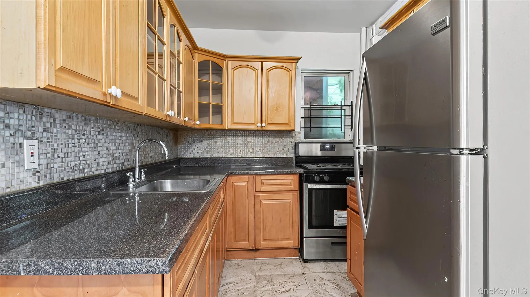 Kitchen featuring stainless steel appliances, backsplash, glass insert cabinets, and dark stone countertops Kitchen featuring stainless steel appliances, backsplash, glass insert cabinets, and dark stone countertops