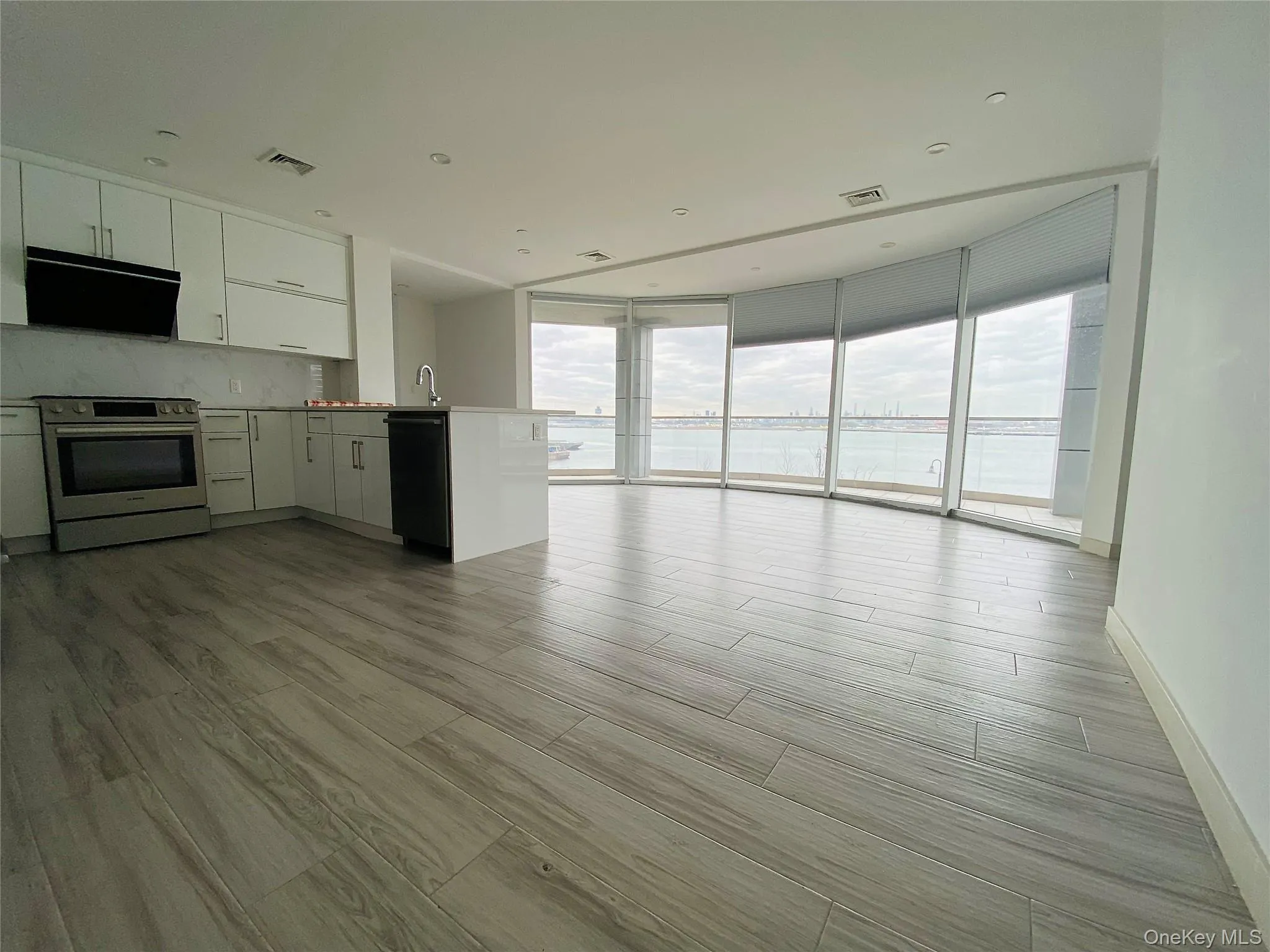 Kitchen with expansive windows, light wood-type flooring, stainless steel electric stove, white cabinets, and open floor plan Kitchen with expansive windows, light wood-type flooring, stainless steel electric stove, white cabinets, and open floor plan