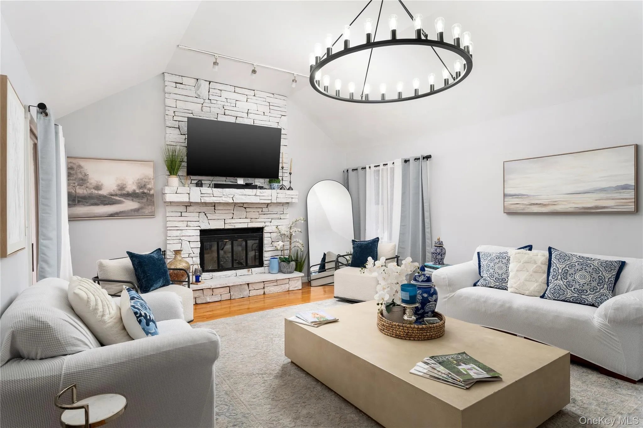 Living area with lofted ceiling, wood finished floors, a stone fireplace, rail lighting, and a chandelier Living area with lofted ceiling, wood finished floors, a stone fireplace, rail lighting, and a chandelier