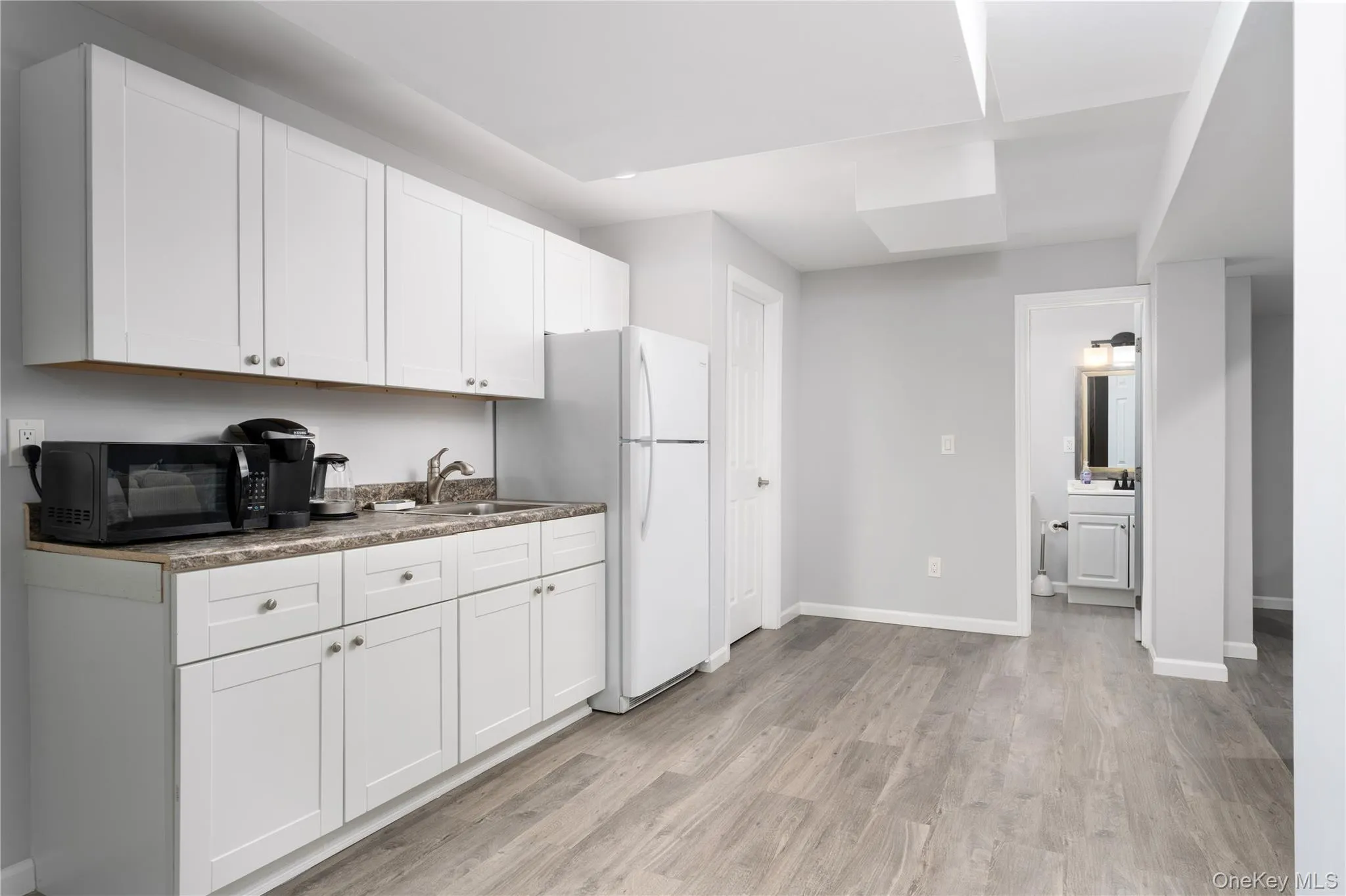 Kitchen featuring light wood-style floors, freestanding refrigerator, white cabinets, and black microwave Kitchen featuring light wood-style floors, freestanding refrigerator, white cabinets, and black microwave