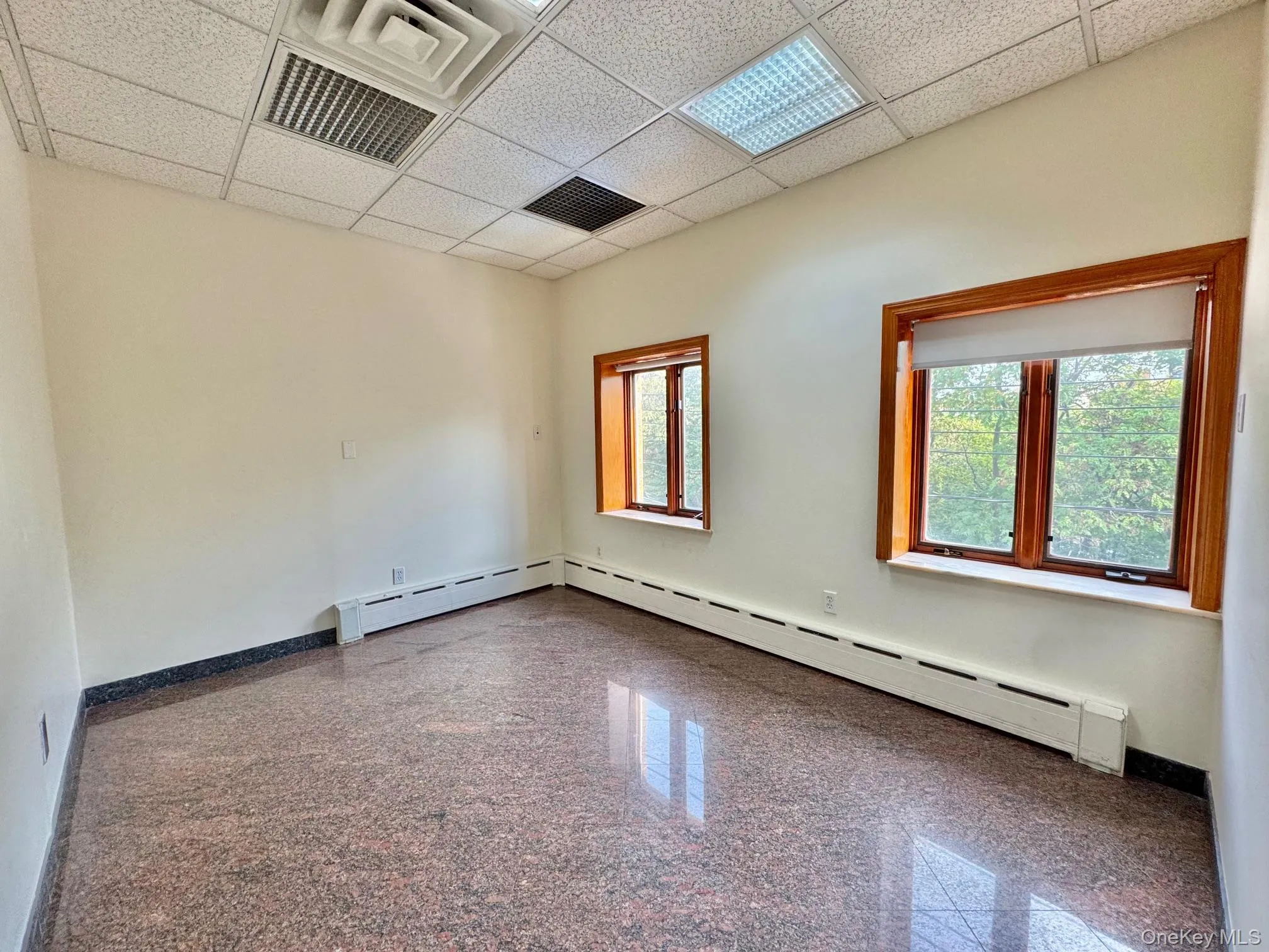 Unfurnished room featuring granite tiled floors, a paneled ceiling, and a baseboard heating unit Unfurnished room featuring granite tiled floors, a paneled ceiling, and a baseboard heating unit