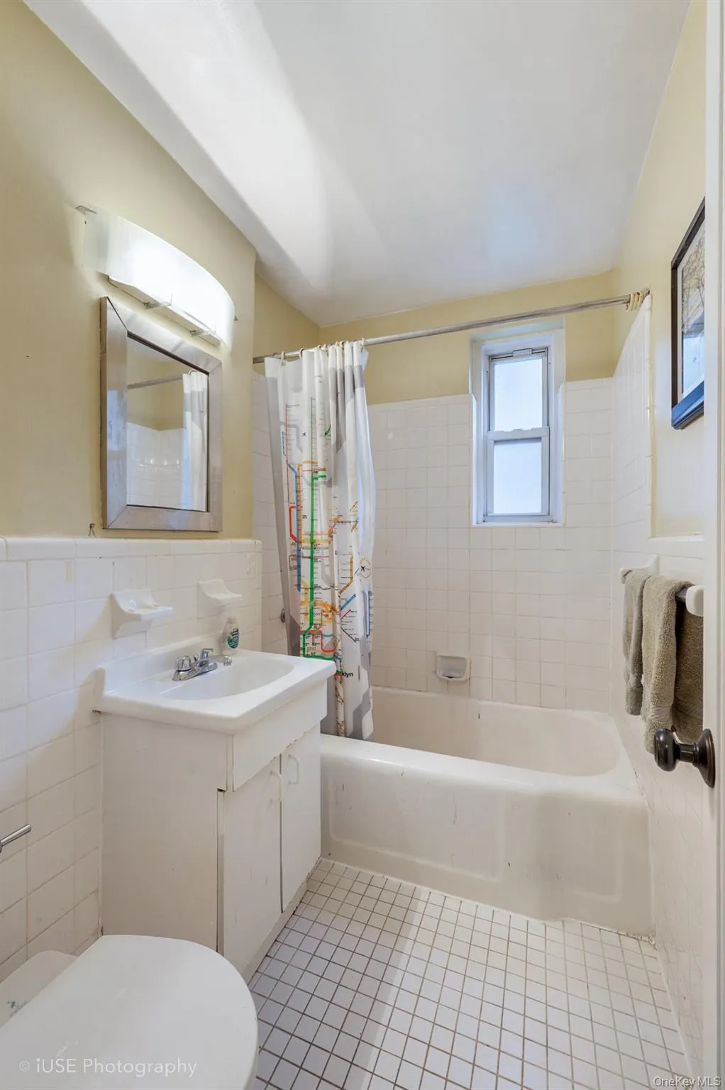 Full bath with shower / bath combo, tile walls, vanity, light tile patterned flooring, and a wainscoted wall Full bath with shower / bath combo, tile walls, vanity, light tile patterned flooring, and a wainscoted wall