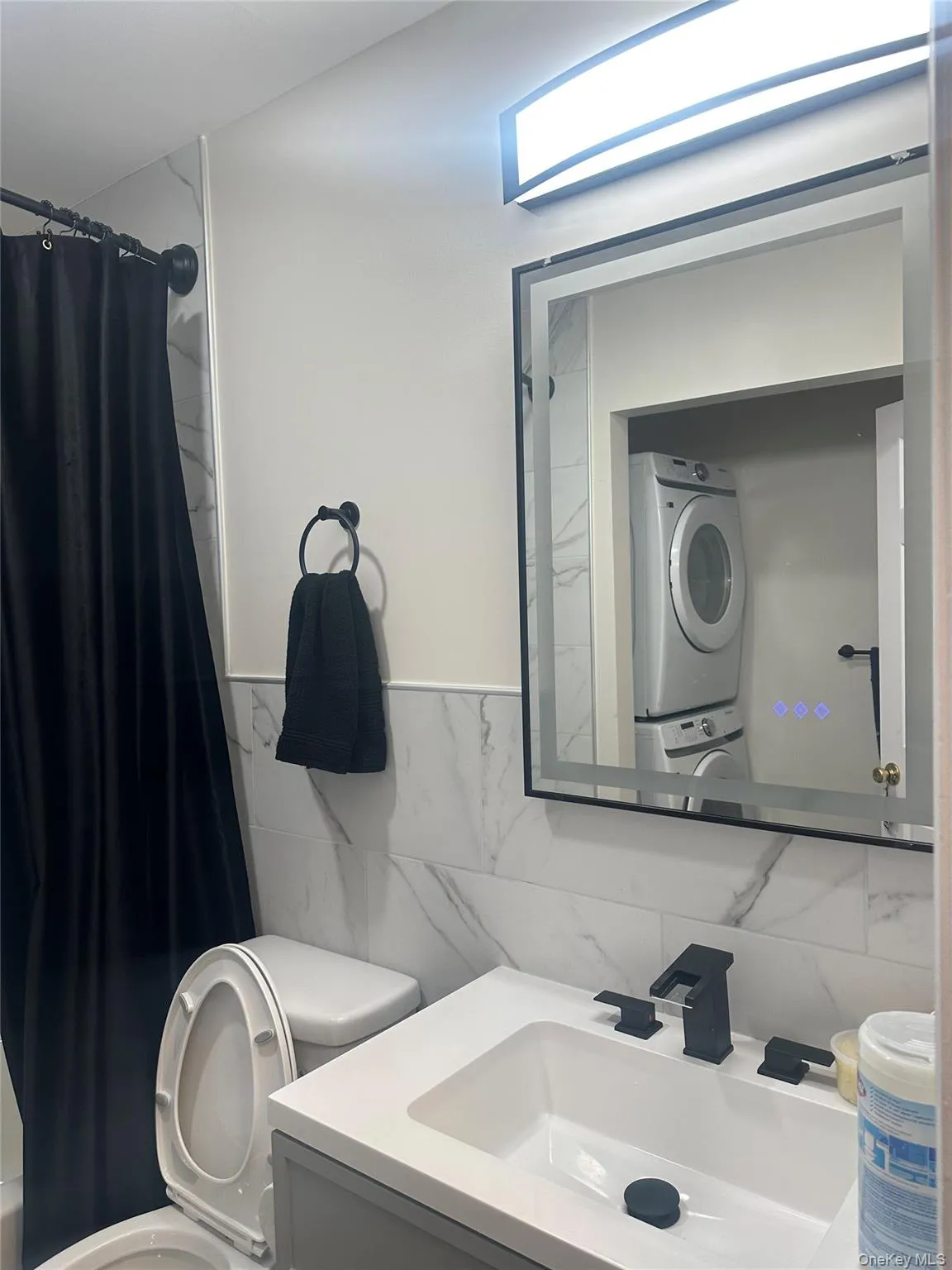 Bathroom featuring vanity, tile walls, shower / bath combo, and stacked washer and clothes dryer Bathroom featuring vanity, tile walls, shower / bath combo, and stacked washer and clothes dryer