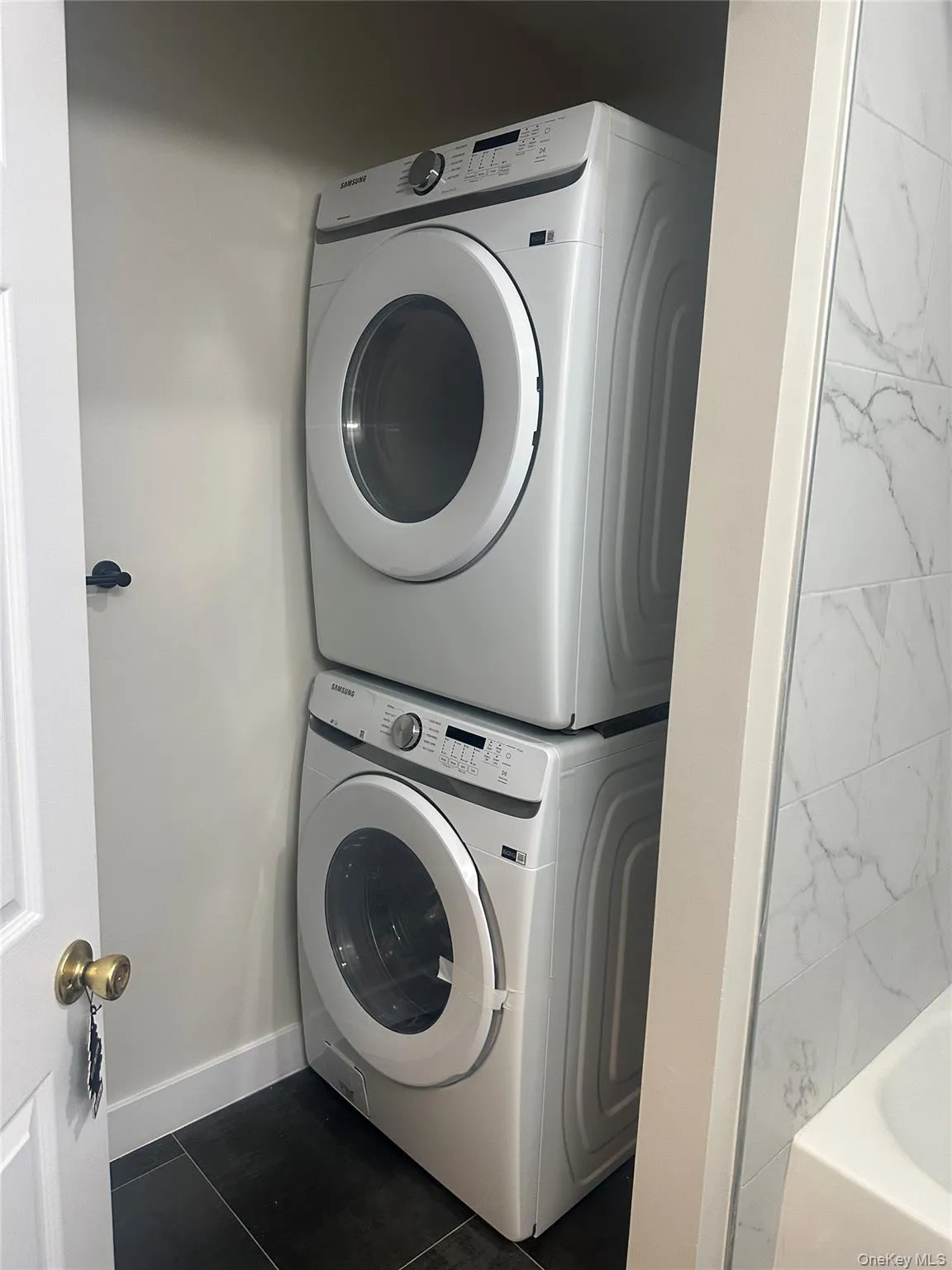 Laundry room featuring estacked washer and dryer and dark tile patterned floors Laundry room featuring estacked washer and dryer and dark tile patterned floors