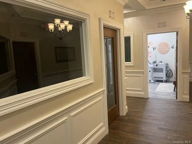 Hall with a chandelier, ornamental molding, dark wood-type flooring, a decorative wall, and coffered ceiling Hall with a chandelier, ornamental molding, dark wood-type flooring, a decorative wall, and coffered ceiling