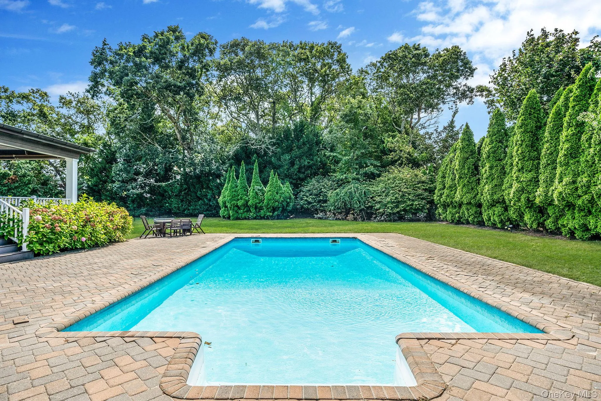 Swimming pool with a yard, a patio area, and view of scattered trees Swimming pool with a yard, a patio area, and view of scattered trees