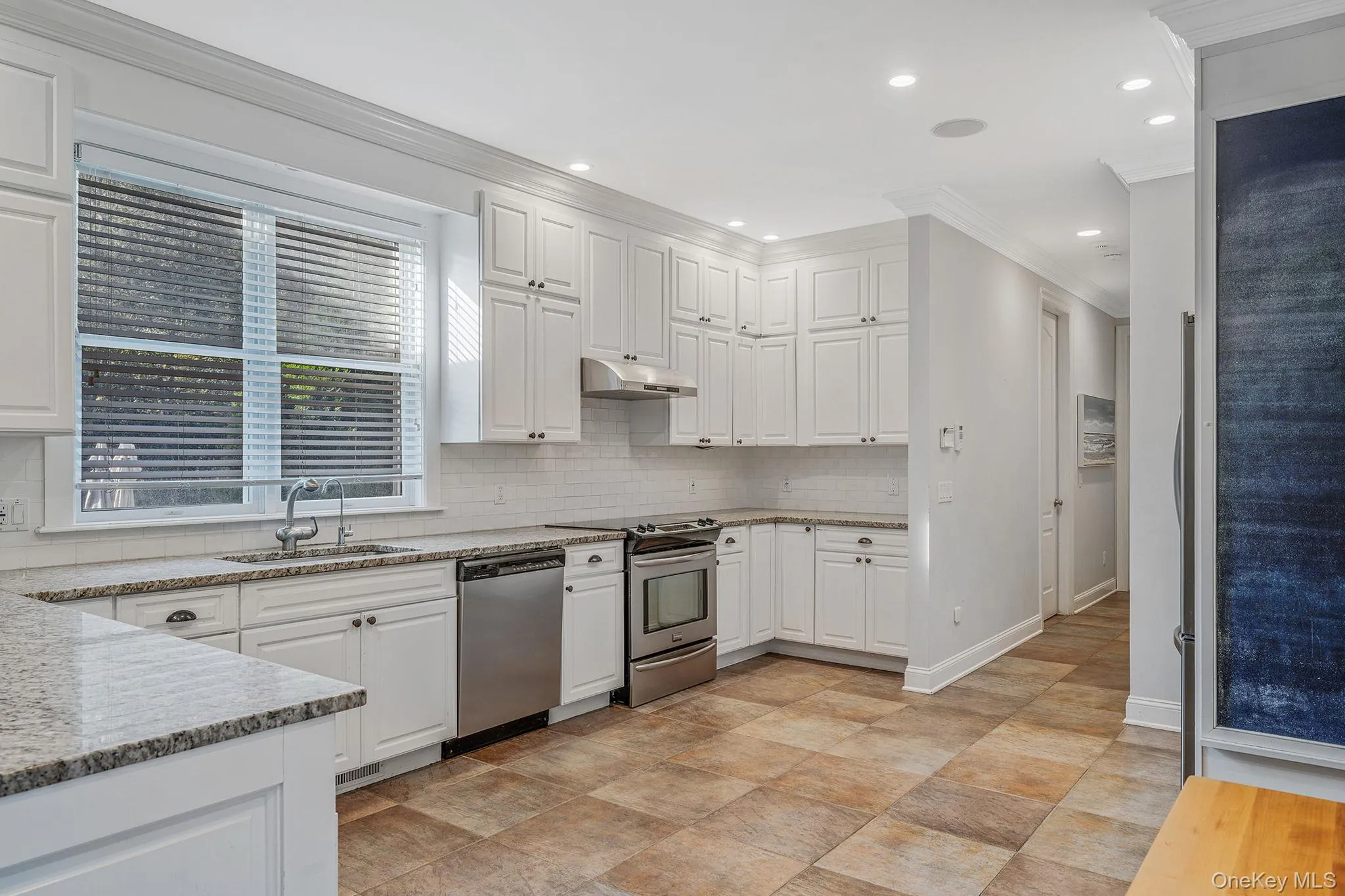 Kitchen featuring appliances with stainless steel finishes, ornamental molding, white cabinetry, light stone countertops, and backsplash Kitchen featuring appliances with stainless steel finishes, ornamental molding, white cabinetry, light stone countertops, and backsplash