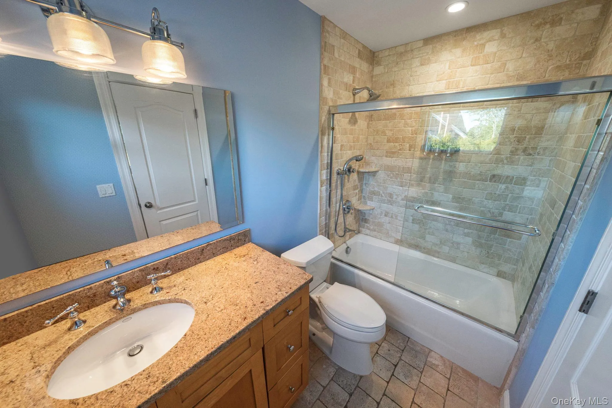 Bathroom with bath / shower combo with glass door, vanity, and dark stone finish floors Bathroom with bath / shower combo with glass door, vanity, and dark stone finish floors