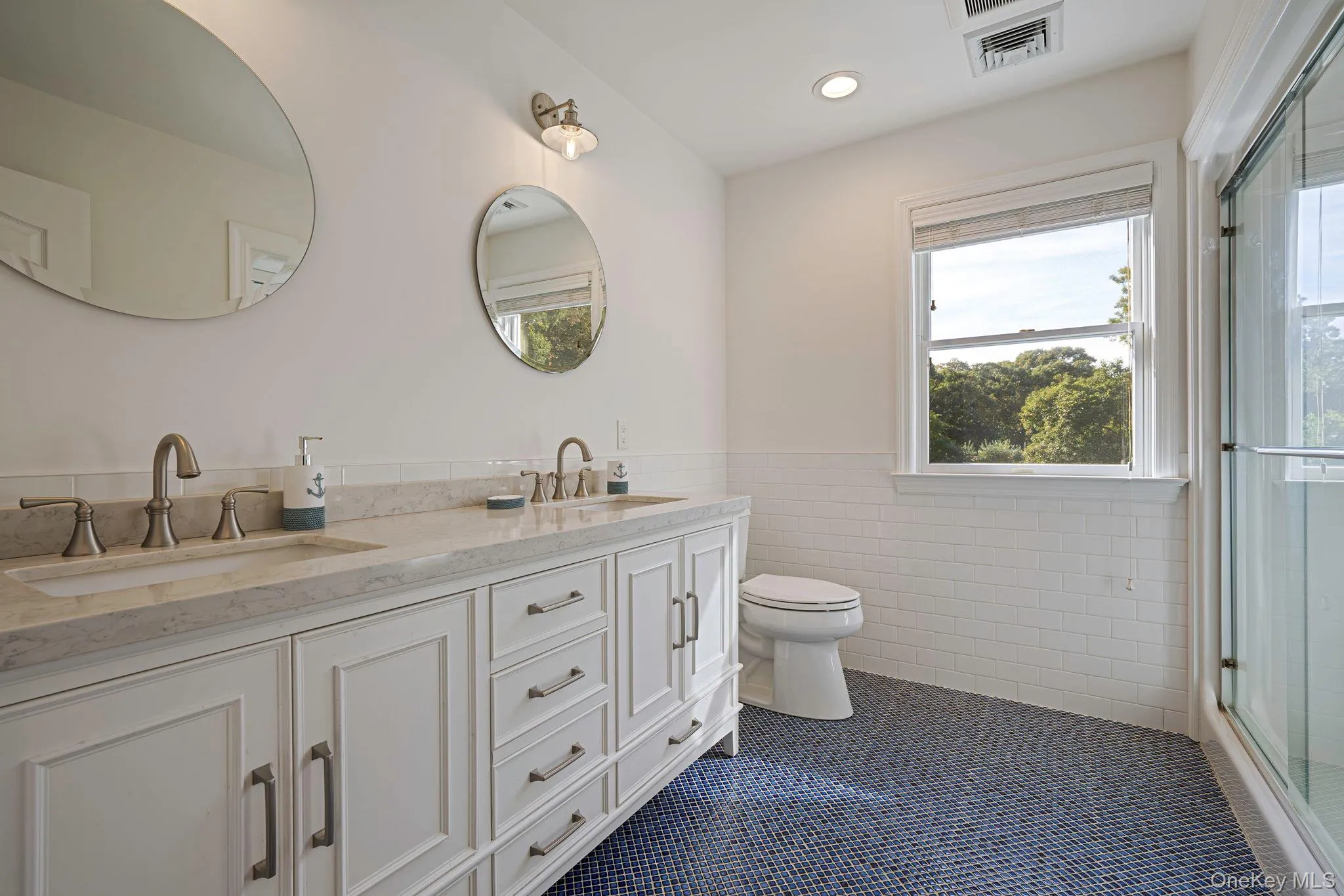 Full bath featuring tile walls, healthy amount of natural light, a stall shower, double vanity, and a wainscoted wall Full bath featuring tile walls, healthy amount of natural light, a stall shower, double vanity, and a wainscoted wall