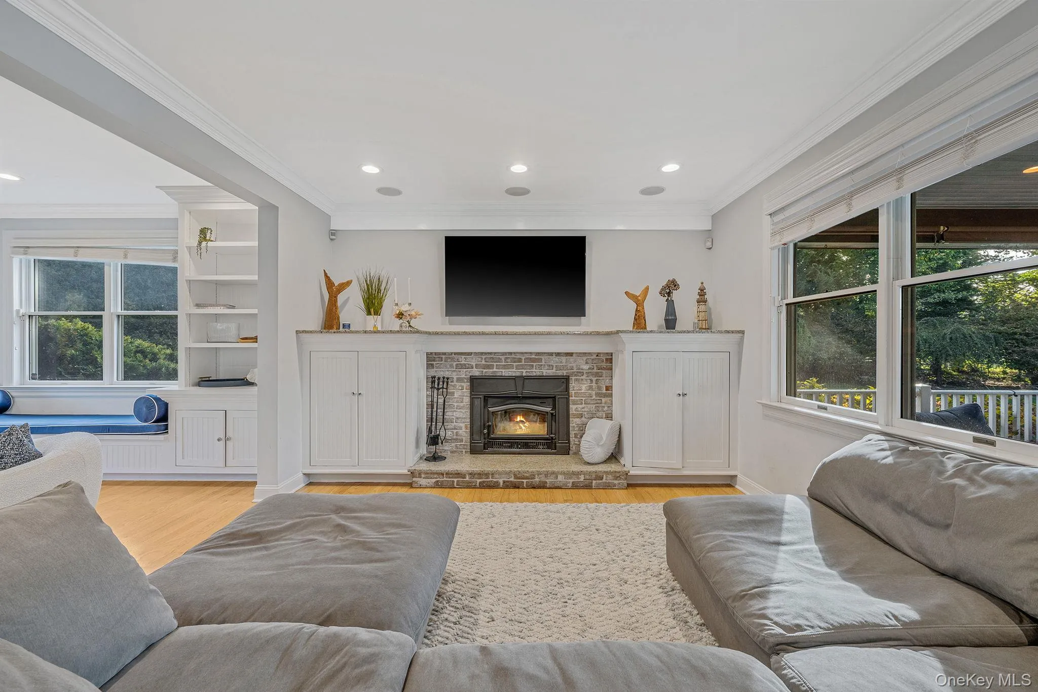 Living area with plenty of natural light, ornamental molding, recessed lighting, light wood-type flooring, and a brick fireplace Living area with plenty of natural light, ornamental molding, recessed lighting, light wood-type flooring, and a brick fireplace