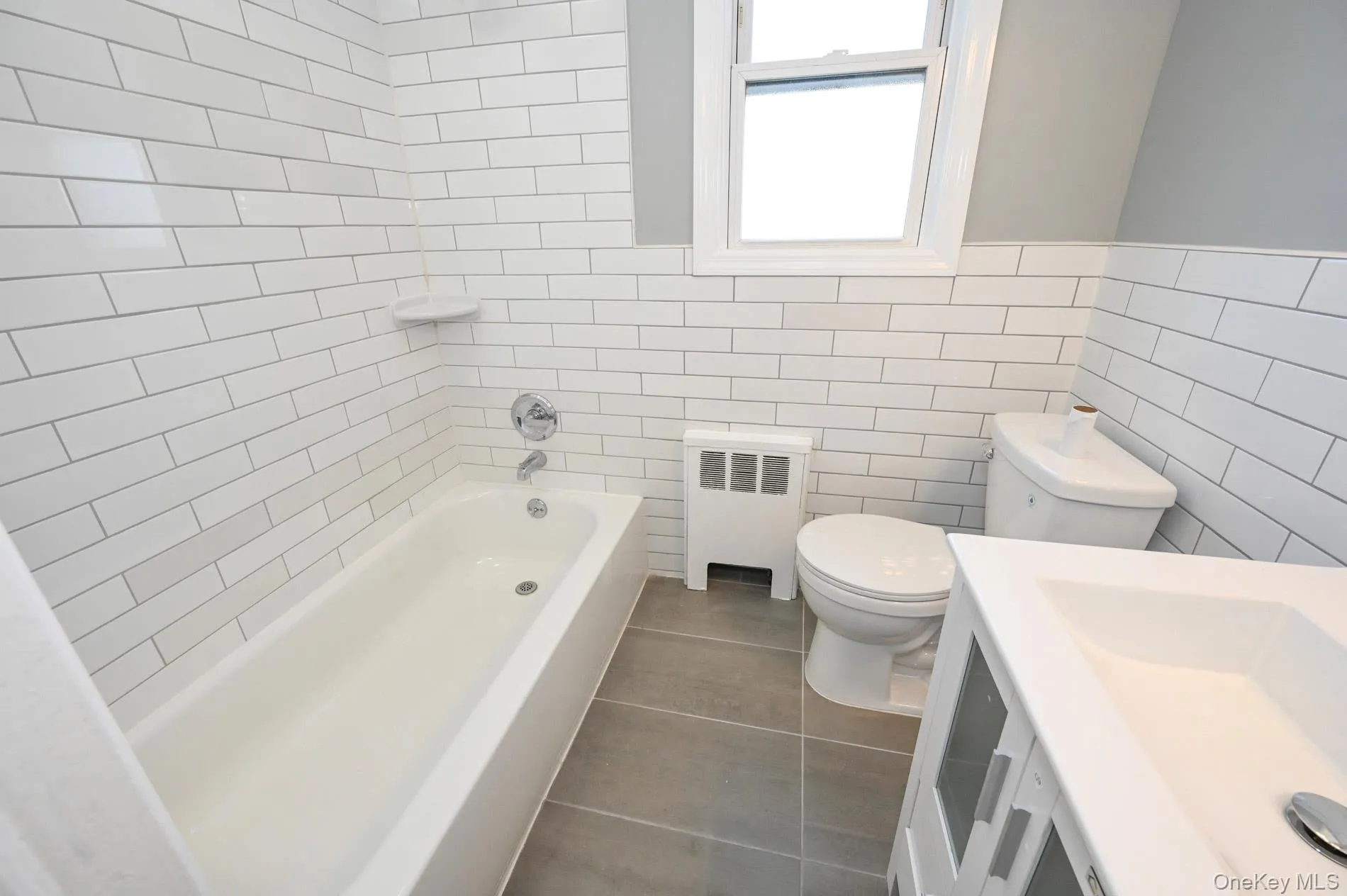 Bathroom with radiator heating unit, vanity, shower / washtub combination, tile walls, and dark tile patterned flooring Bathroom with radiator heating unit, vanity, shower / washtub combination, tile walls, and dark tile patterned flooring