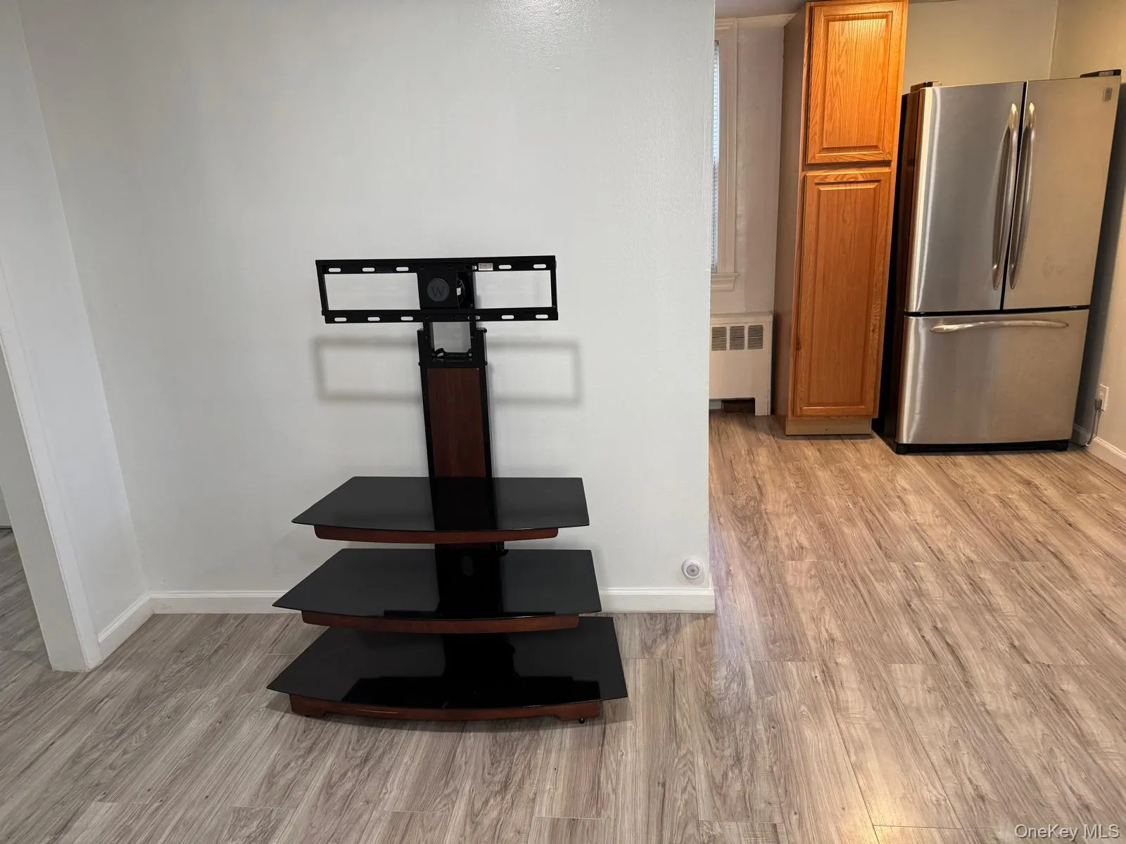 Kitchen view of freestanding refrigerator, brown cabinetry, light wood-style floors, and radiator heating unit Kitchen view of freestanding refrigerator, brown cabinetry, light wood-style floors, and radiator heating unit