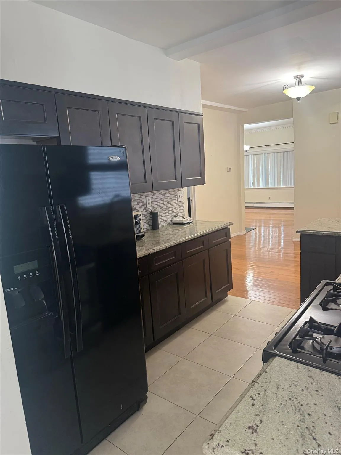 Kitchen with black appliances, light stone counters, light tile patterned floors, tasteful backsplash, and dark brown cabinets Kitchen with black appliances, light stone counters, light tile patterned floors, tasteful backsplash, and dark brown cabinets