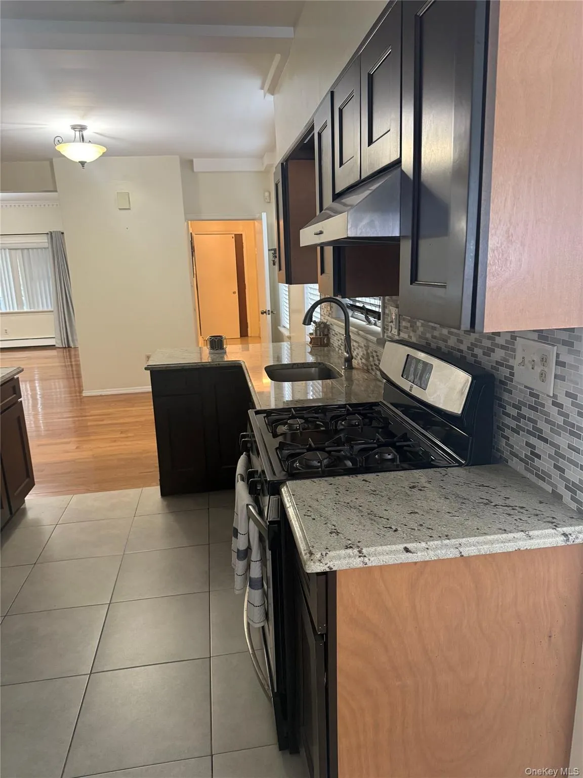 Kitchen with stainless steel gas range, light tile patterned flooring, light stone counters, under cabinet range hood, and decorative backsplash Kitchen with stainless steel gas range, light tile patterned flooring, light stone counters, under cabinet range hood, and decorative backsplash