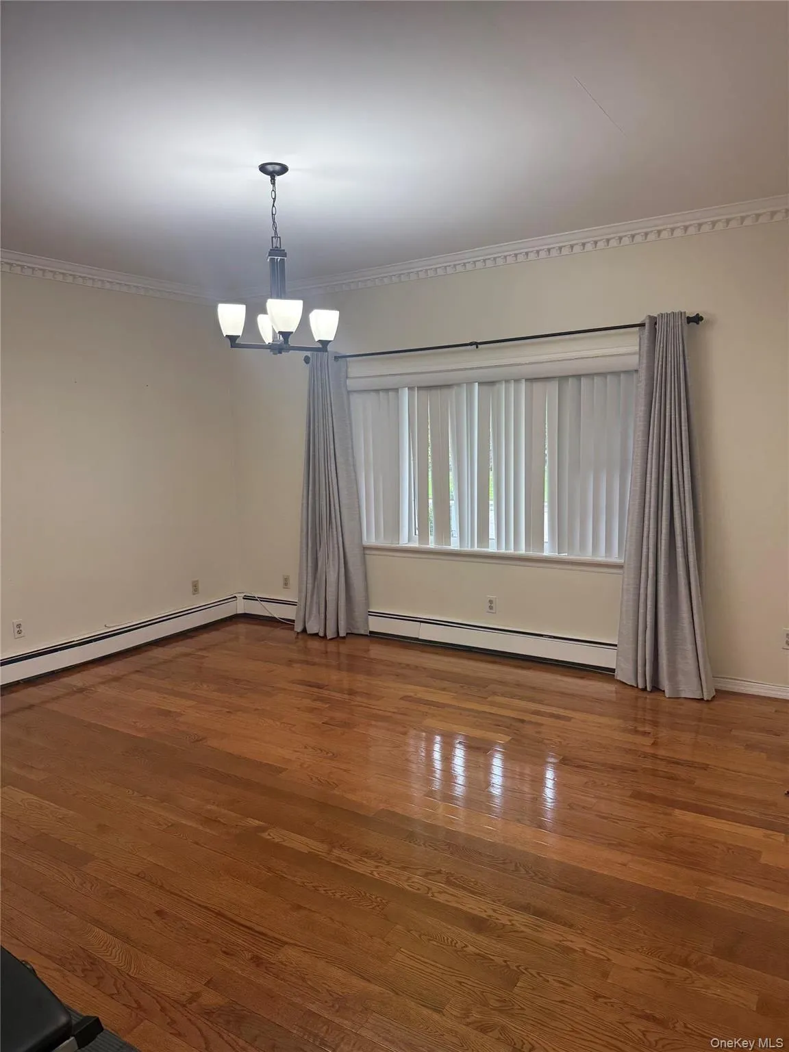 Empty room featuring wood finished floors, ornamental molding, a chandelier, and a baseboard heating unit Empty room featuring wood finished floors, ornamental molding, a chandelier, and a baseboard heating unit