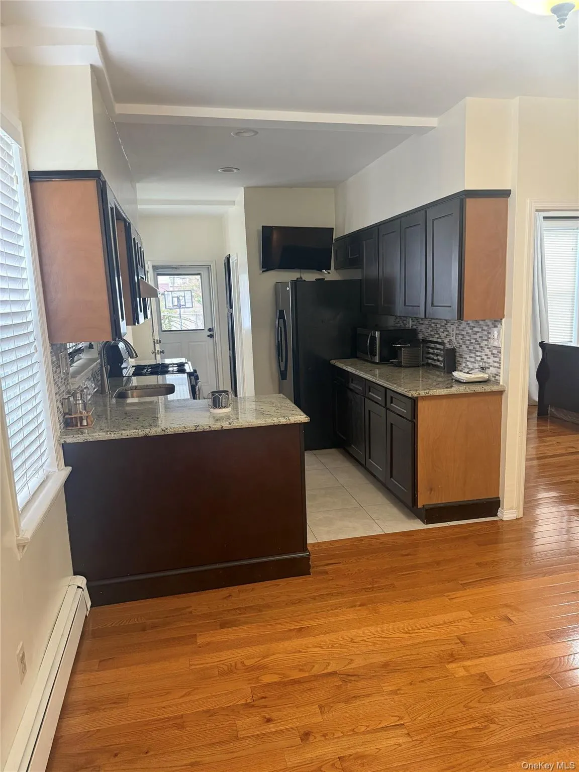 Kitchen with light stone counters, a baseboard radiator, light wood finished floors, and a peninsula Kitchen with light stone counters, a baseboard radiator, light wood finished floors, and a peninsula