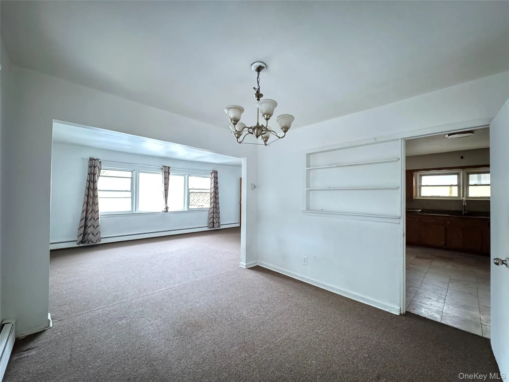 Unfurnished room with plenty of natural light, carpet, a chandelier, and baseboard heating Unfurnished room with plenty of natural light, carpet, a chandelier, and baseboard heating
