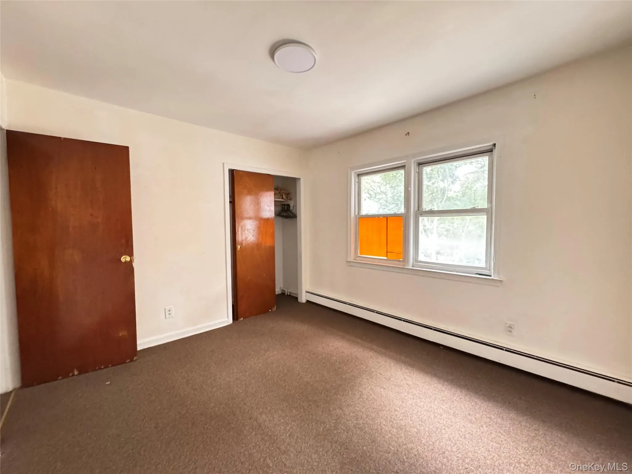 Unfurnished bedroom with baseboard heating, carpet, and a closet Unfurnished bedroom with baseboard heating, carpet, and a closet