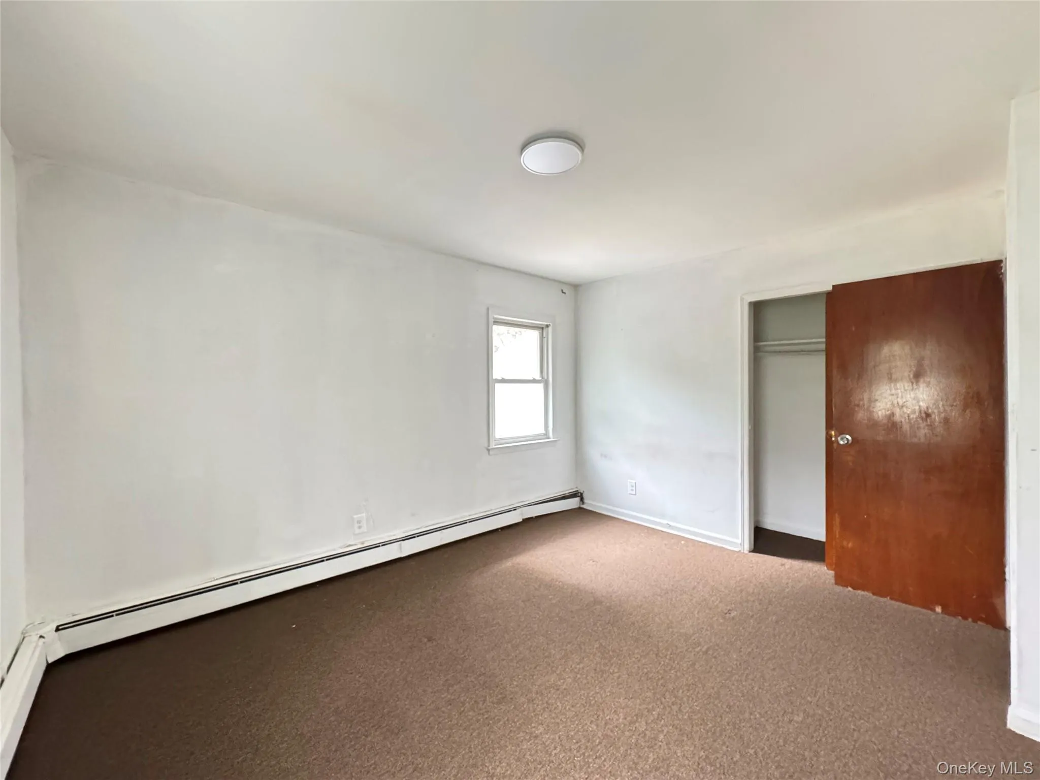 Unfurnished bedroom featuring a baseboard heating unit, carpet floors, and a closet Unfurnished bedroom featuring a baseboard heating unit, carpet floors, and a closet