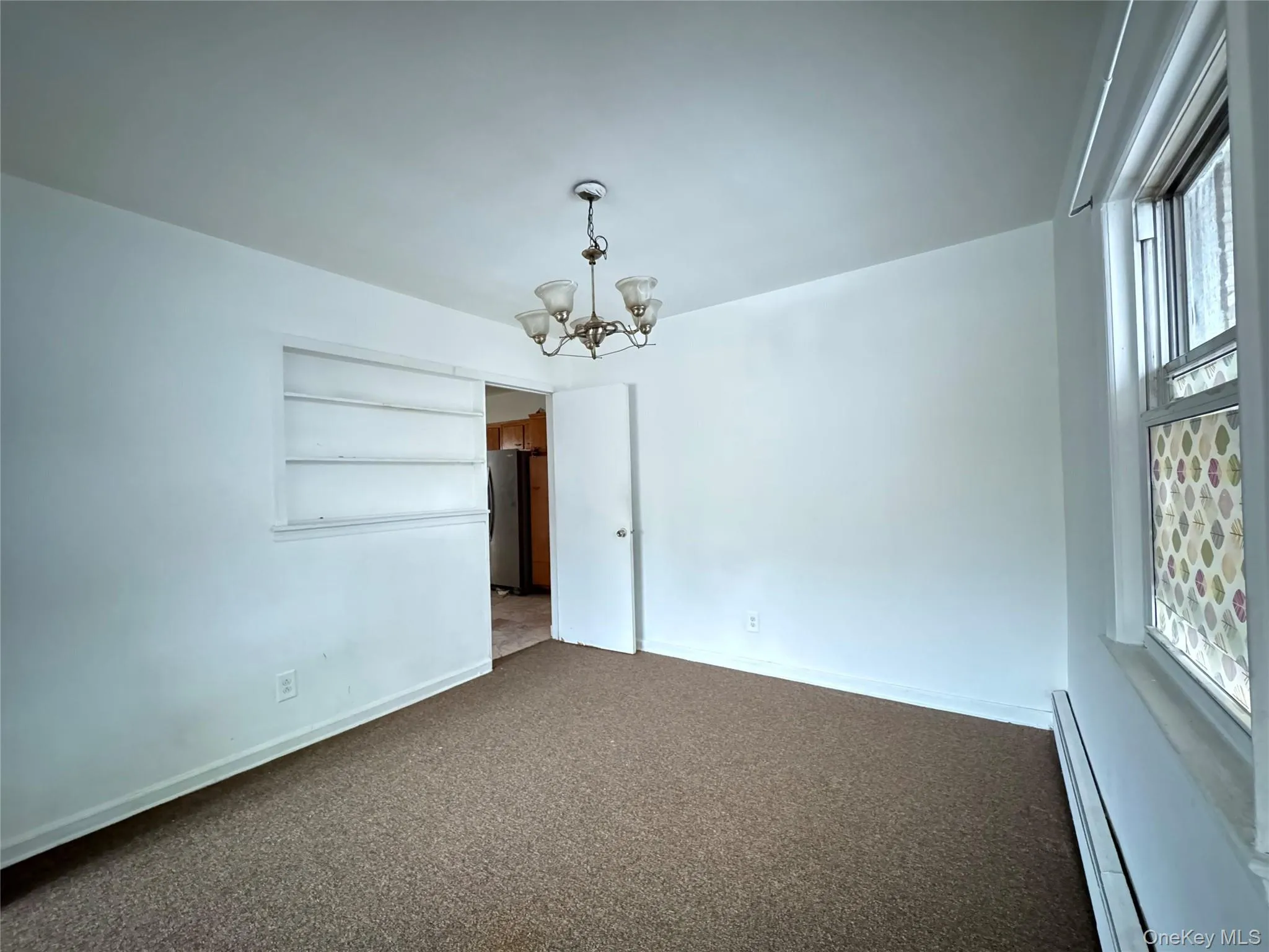 Carpeted spare room with a baseboard heating unit, a chandelier, and built in features Carpeted spare room with a baseboard heating unit, a chandelier, and built in features