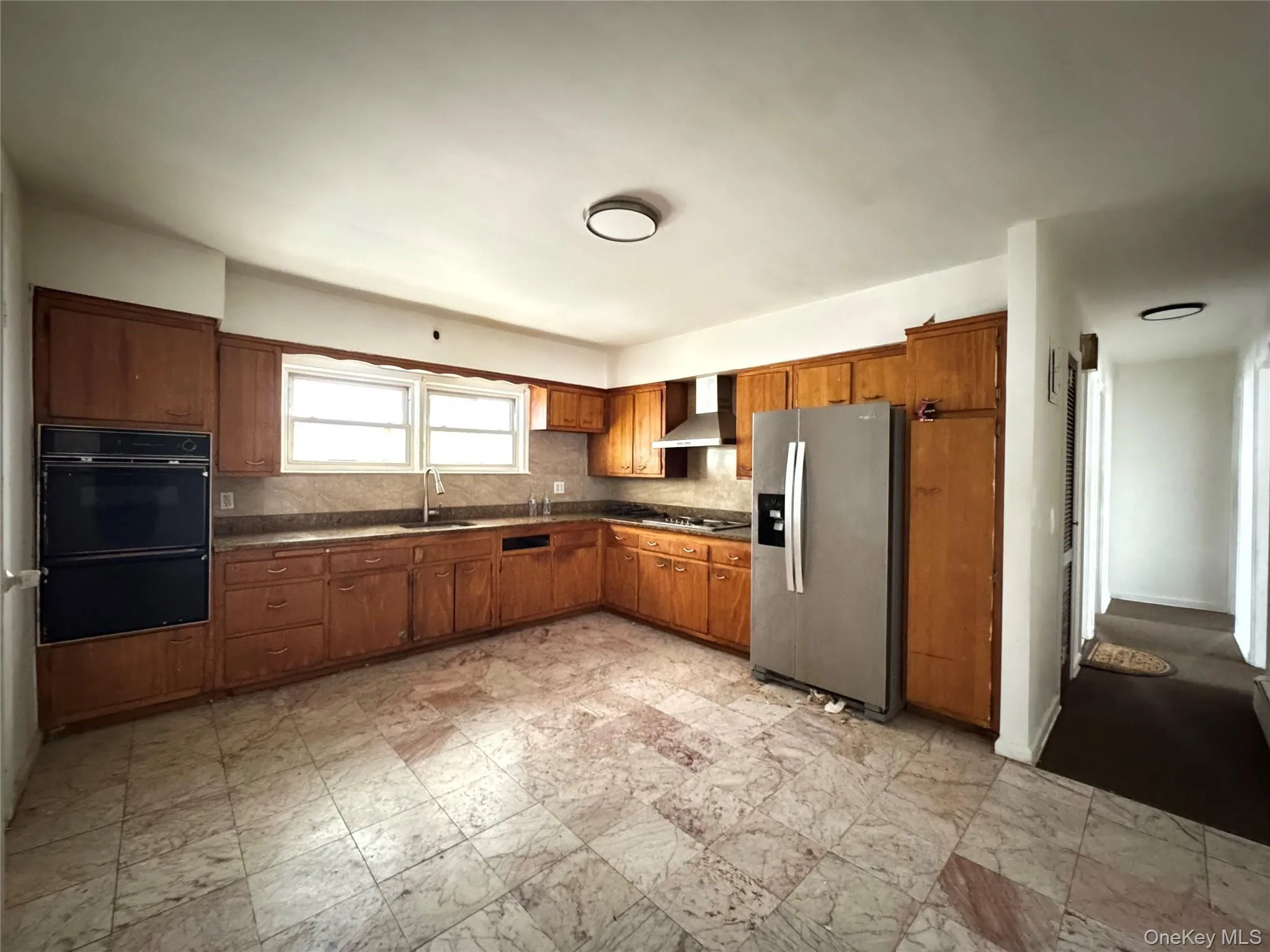 Kitchen featuring dark countertops, black appliances, backsplash, brown cabinetry, and wall chimney exhaust hood Kitchen featuring dark countertops, black appliances, backsplash, brown cabinetry, and wall chimney exhaust hood