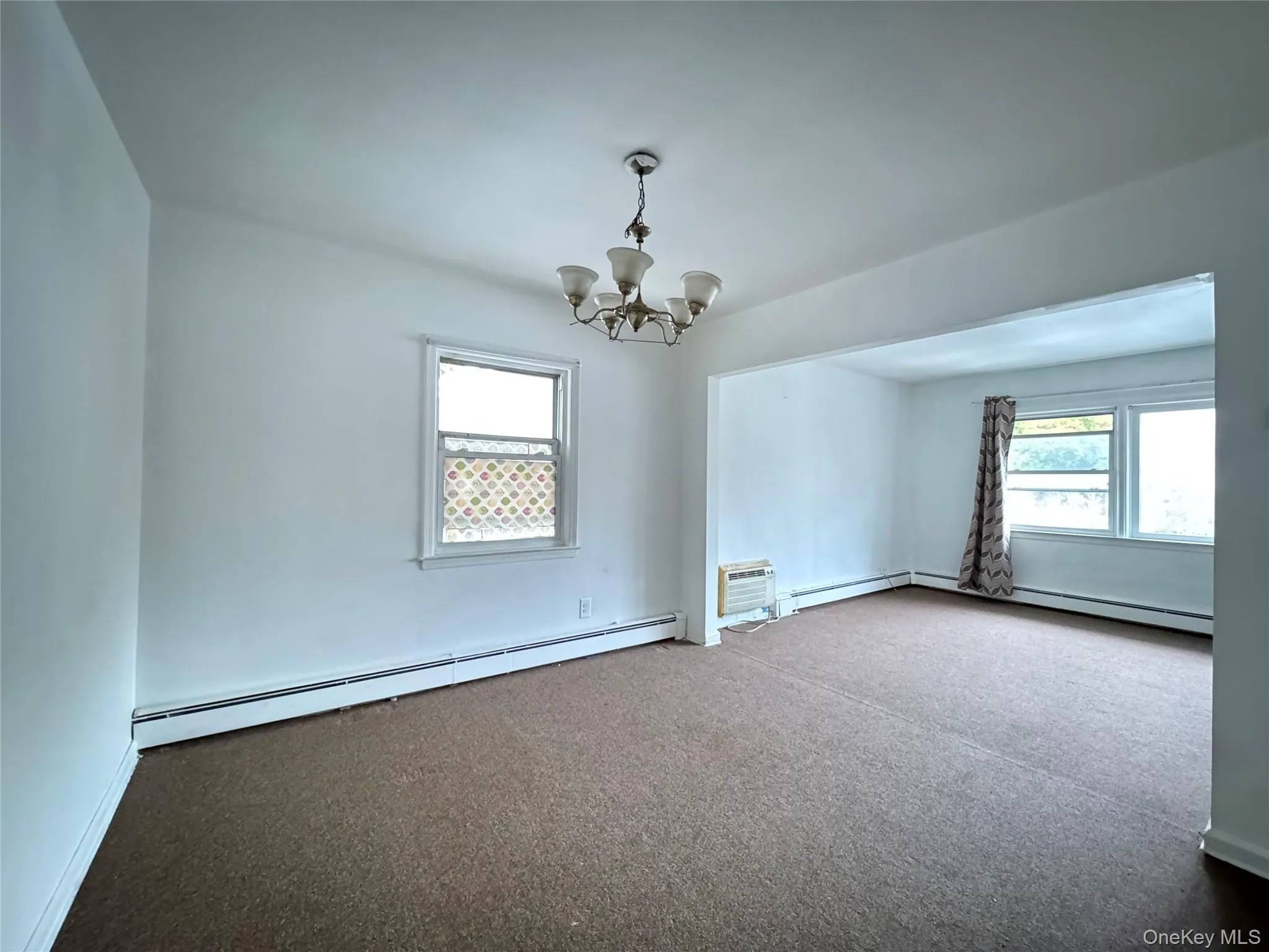 Carpeted spare room with a baseboard heating unit, a chandelier, and a wall mounted AC Carpeted spare room with a baseboard heating unit, a chandelier, and a wall mounted AC