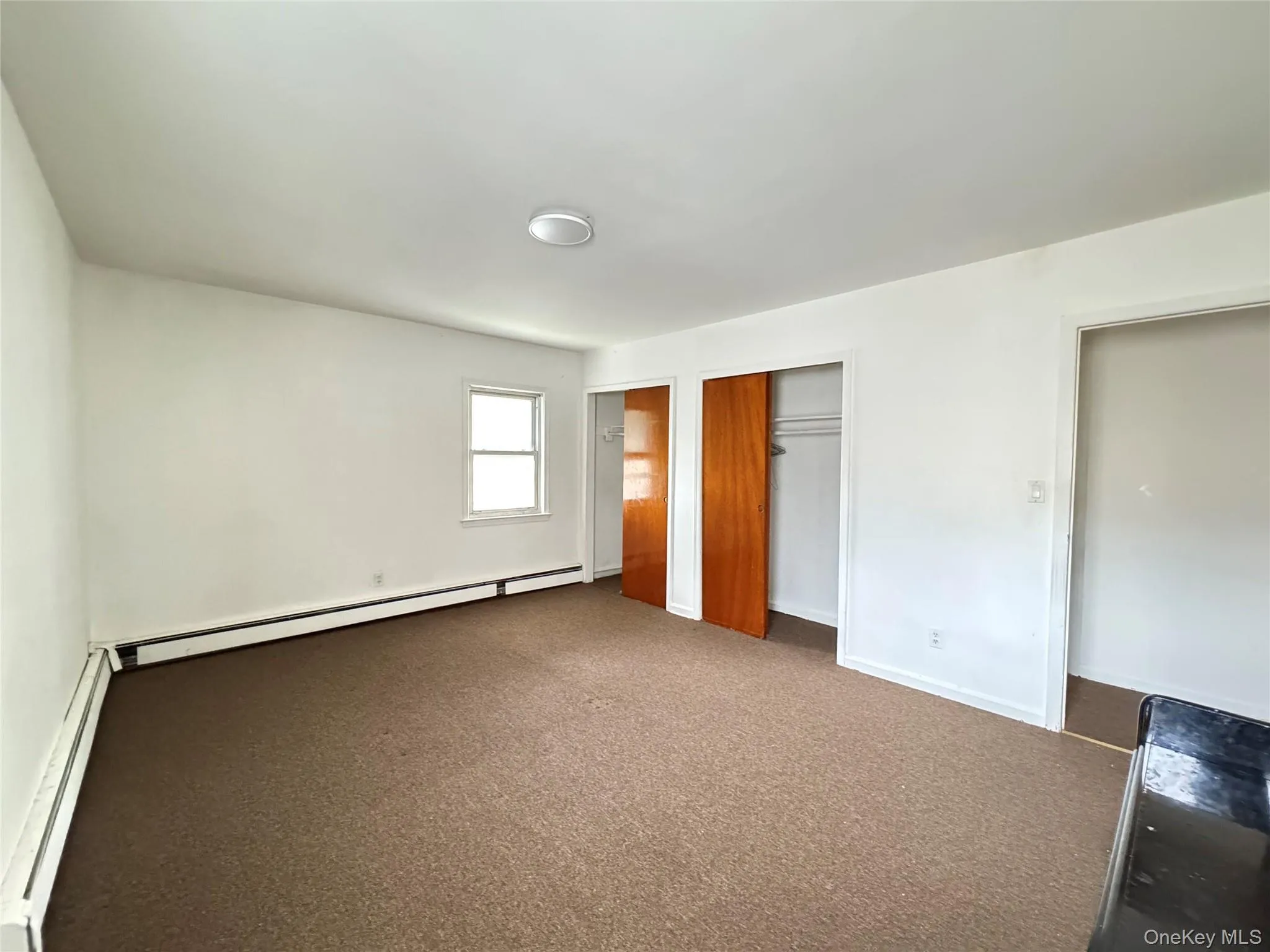 Unfurnished bedroom with a baseboard radiator, two closets, and carpet Unfurnished bedroom with a baseboard radiator, two closets, and carpet