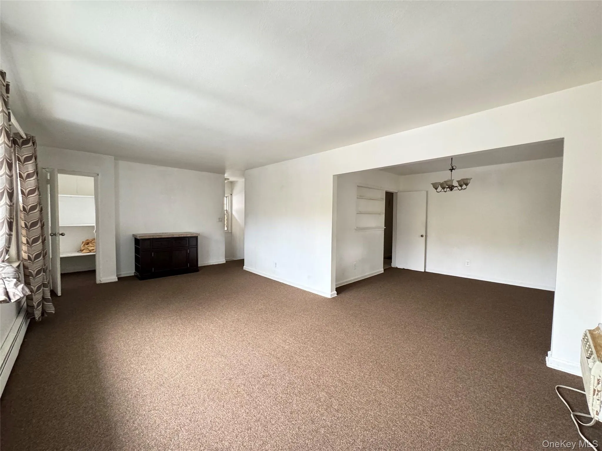 Unfurnished living room with carpet flooring, a chandelier, and a baseboard heating unit Unfurnished living room with carpet flooring, a chandelier, and a baseboard heating unit