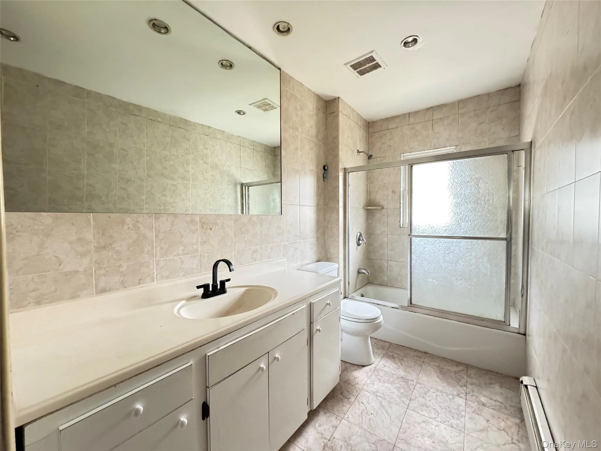 Bathroom featuring tile walls, a baseboard radiator, vanity, combined bath / shower with glass door, and recessed lighting Bathroom featuring tile walls, a baseboard radiator, vanity, combined bath / shower with glass door, and recessed lighting