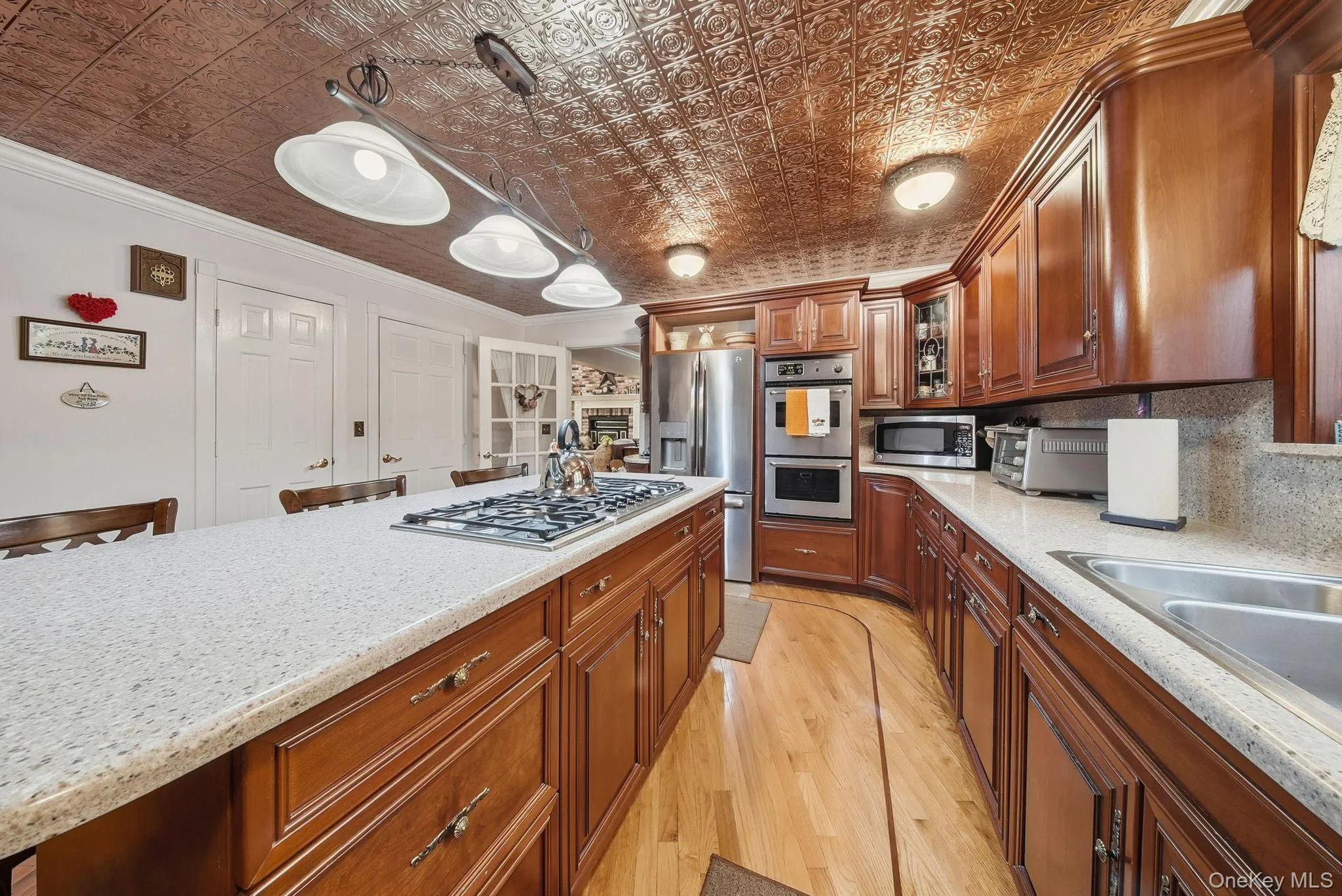 Kitchen with brown cabinets, stainless steel appliances, pendant lighting, glass insert cabinets, and light wood-style flooring Kitchen with brown cabinets, stainless steel appliances, pendant lighting, glass insert cabinets, and light wood-style flooring