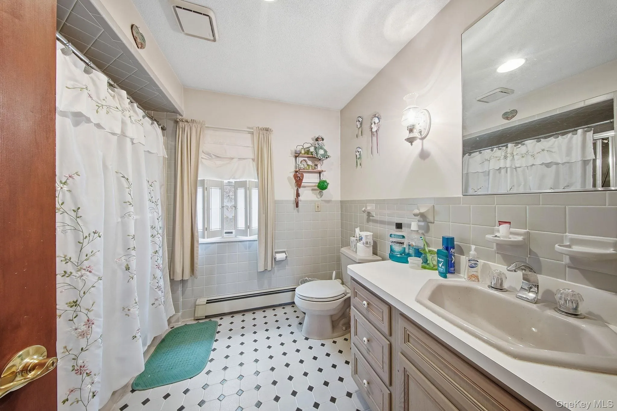 Full bath with tile walls, curtained shower, a baseboard radiator, vanity, and a wainscoted wall Full bath with tile walls, curtained shower, a baseboard radiator, vanity, and a wainscoted wall