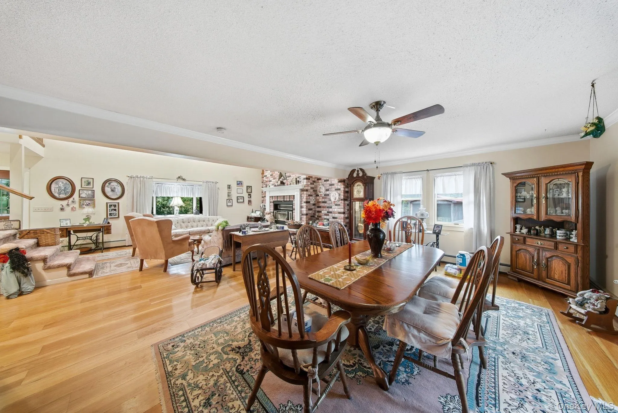 Dining area with light wood-type flooring, a textured ceiling, ornamental molding, ceiling fan, and a brick fireplace Dining area with light wood-type flooring, a textured ceiling, ornamental molding, ceiling fan, and a brick fireplace