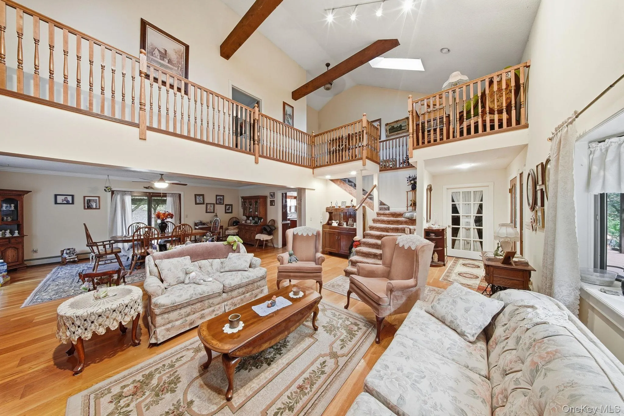 Living area featuring light wood finished floors, a skylight, beam ceiling, high vaulted ceiling, and a ceiling fan Living area featuring light wood finished floors, a skylight, beam ceiling, high vaulted ceiling, and a ceiling fan