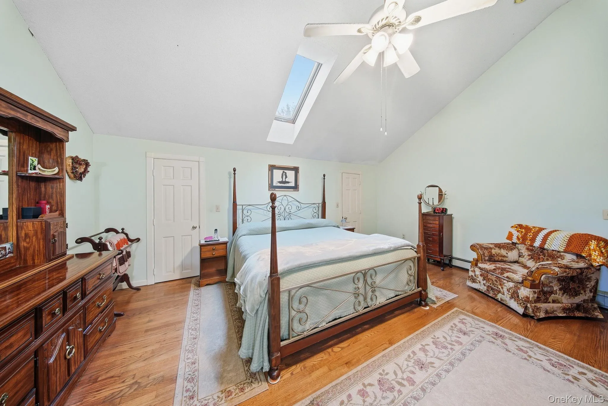 Bedroom with light wood finished floors, vaulted ceiling, ceiling fan, and a skylight Bedroom with light wood finished floors, vaulted ceiling, ceiling fan, and a skylight
