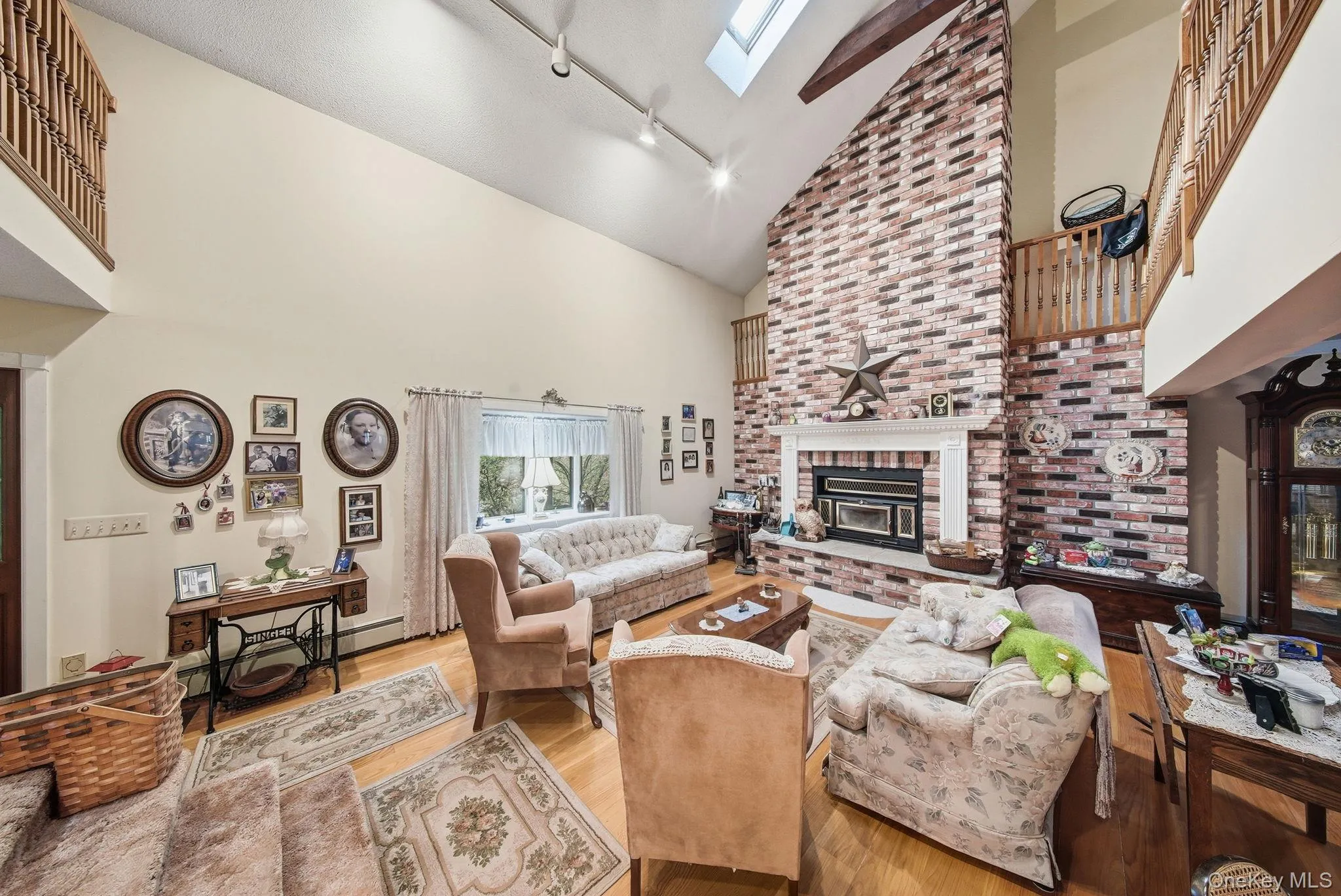 Living room with high vaulted ceiling, a brick fireplace, track lighting, wood finished floors, and a skylight Living room with high vaulted ceiling, a brick fireplace, track lighting, wood finished floors, and a skylight