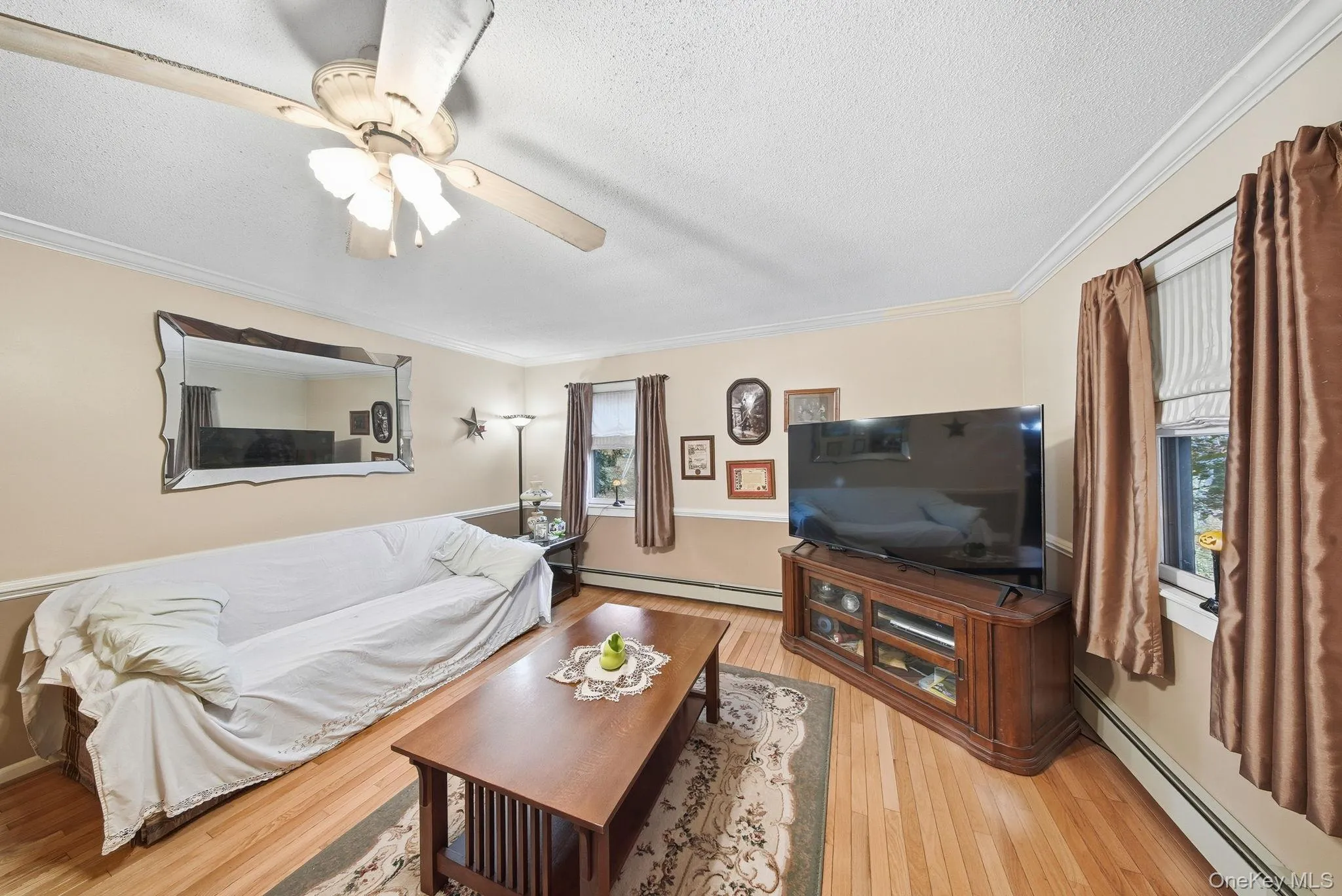 Den Living Area featuring a baseboard radiator, light wood-type flooring, a textured ceiling, crown molding, and ceiling fan Den Living Area featuring a baseboard radiator, light wood-type flooring, a textured ceiling, crown molding, and ceiling fan