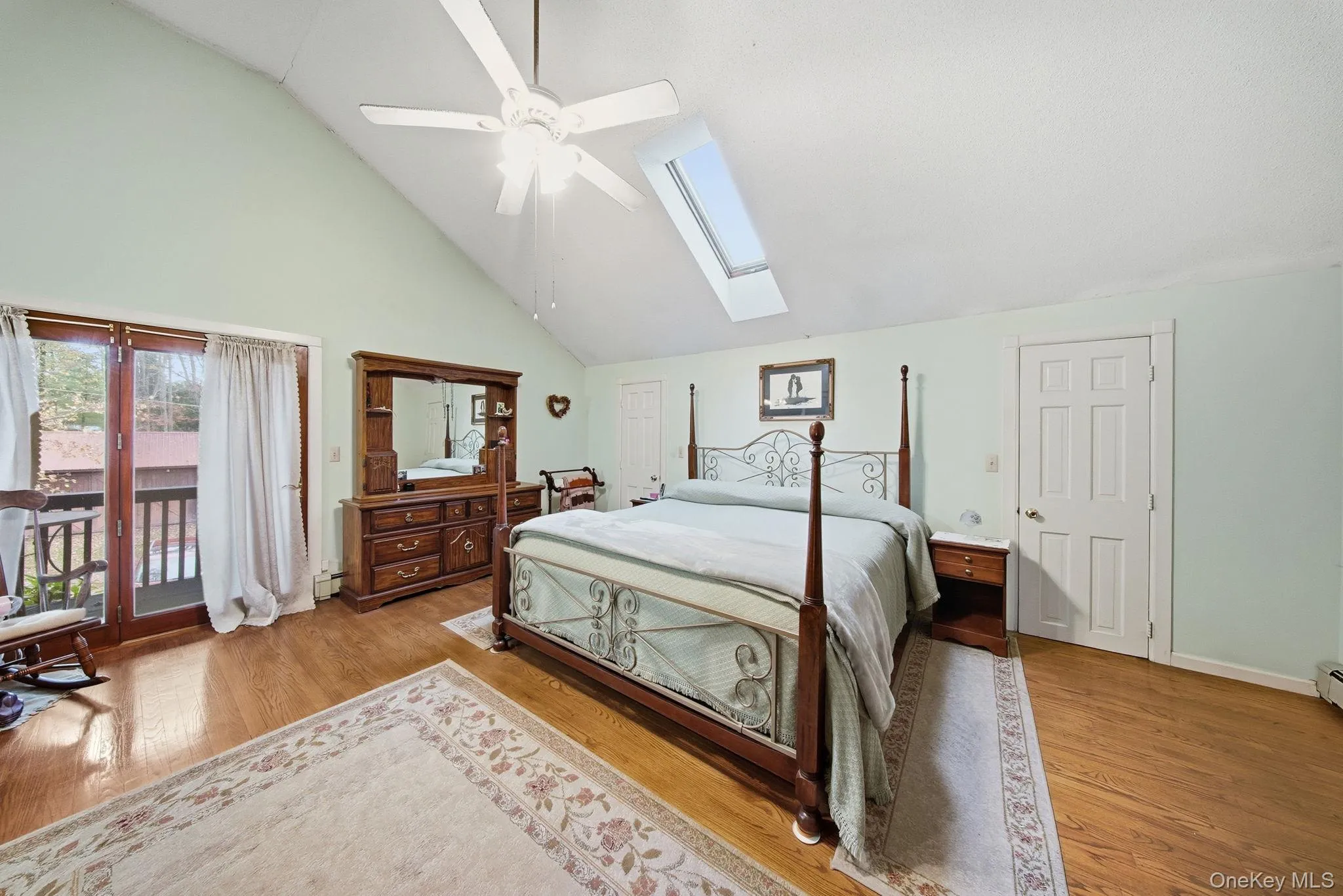 Bedroom featuring access to outside, a skylight, high vaulted ceiling, light wood finished floors, and a ceiling fan Bedroom featuring access to outside, a skylight, high vaulted ceiling, light wood finished floors, and a ceiling fan