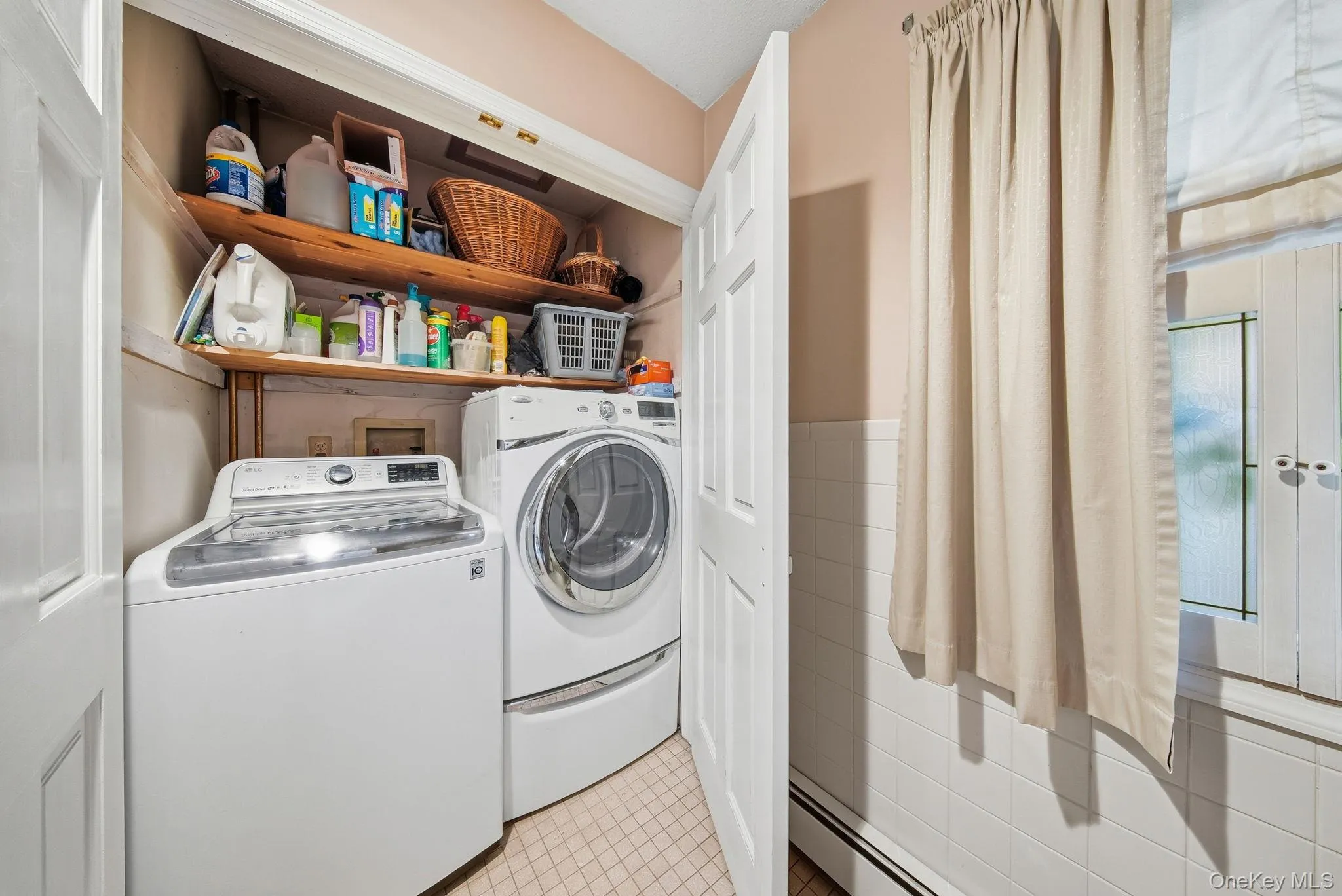 Laundry area featuring light tile patterned floors, baseboard heating, independent washer and dryer, tile walls, and a wainscoted wall Laundry area featuring light tile patterned floors, baseboard heating, independent washer and dryer, tile walls, and a wainscoted wall