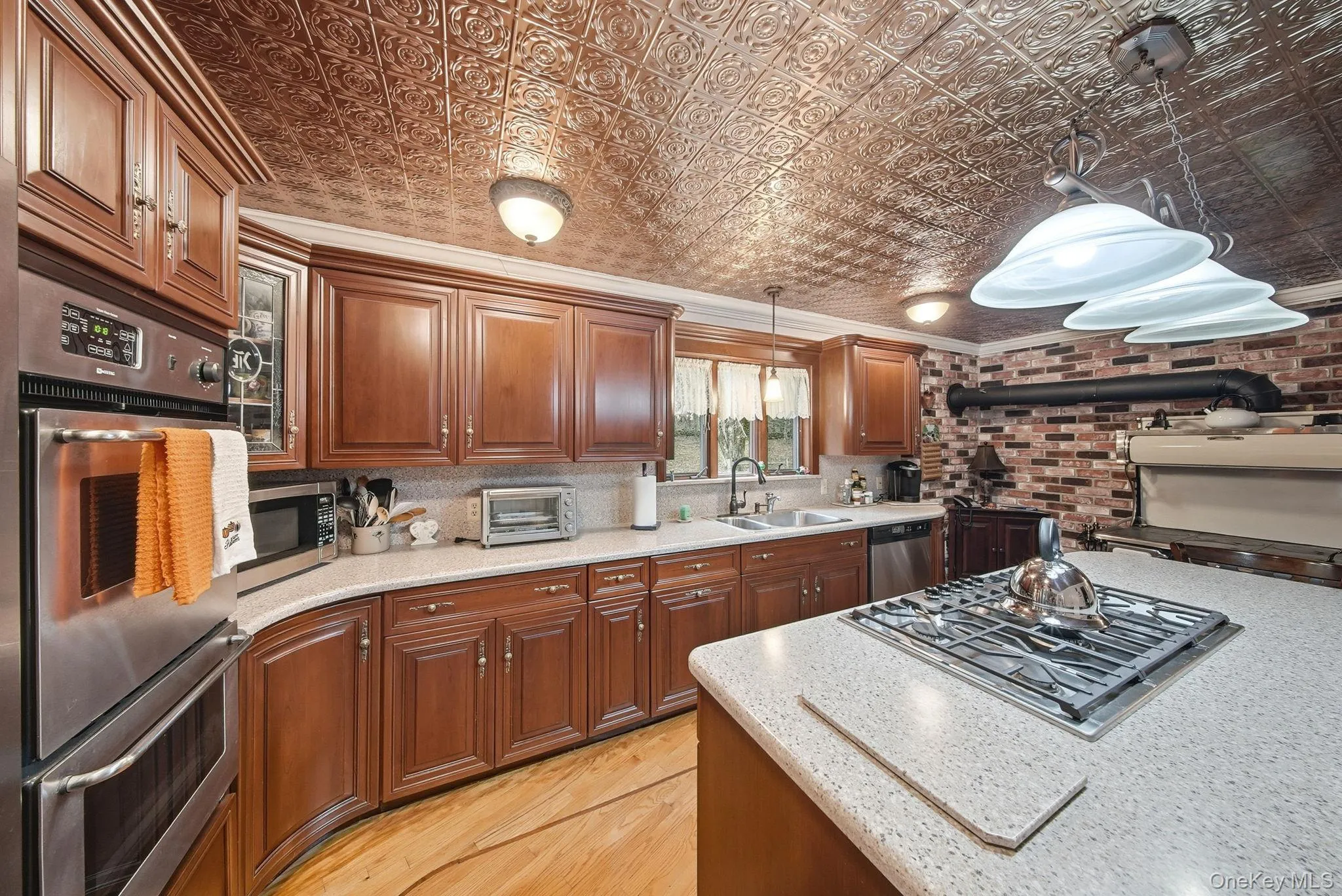 Kitchen with stainless steel appliances, hanging light fixtures, brown cabinets, ornamental molding, and an ornate ceiling Kitchen with stainless steel appliances, hanging light fixtures, brown cabinets, ornamental molding, and an ornate ceiling
