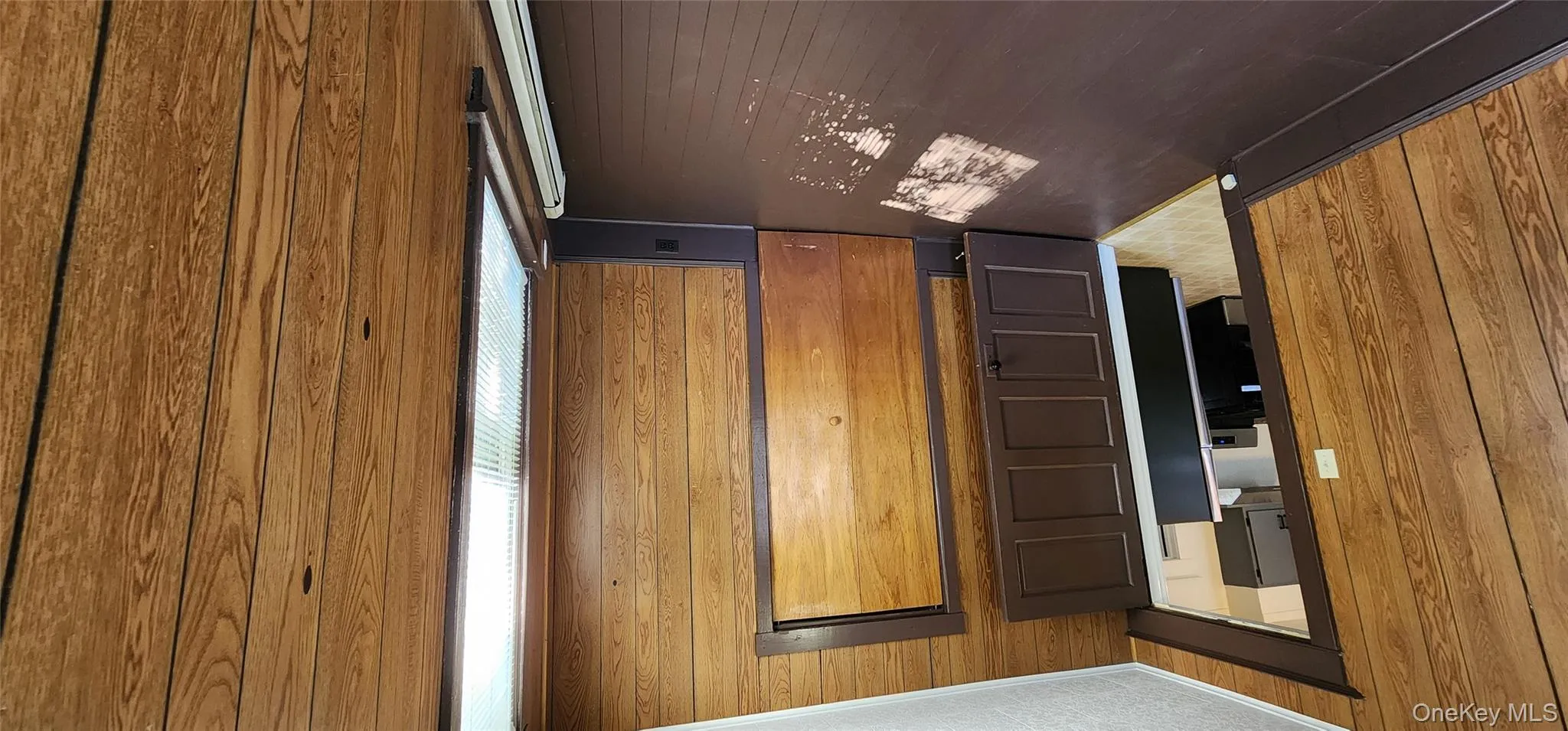 Unfurnished bedroom featuring wooden walls, crown molding, dark wood finished floors, a baseboard radiator, and refrigerator Unfurnished bedroom featuring wooden walls, crown molding, dark wood finished floors, a baseboard radiator, and refrigerator