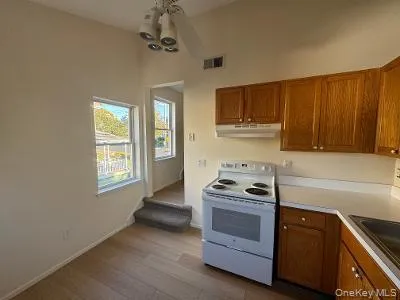 Kitchen with brown cabinets, electric stove, light countertops, light wood finished floors, and under cabinet range hood Kitchen with brown cabinets, electric stove, light countertops, light wood finished floors, and under cabinet range hood
