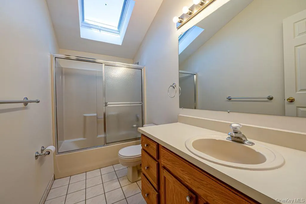 Bathroom with vanity, light tile patterned floors, shower / bath combination with glass door, a skylight, and vaulted ceiling Bathroom with vanity, light tile patterned floors, shower / bath combination with glass door, a skylight, and vaulted ceiling
