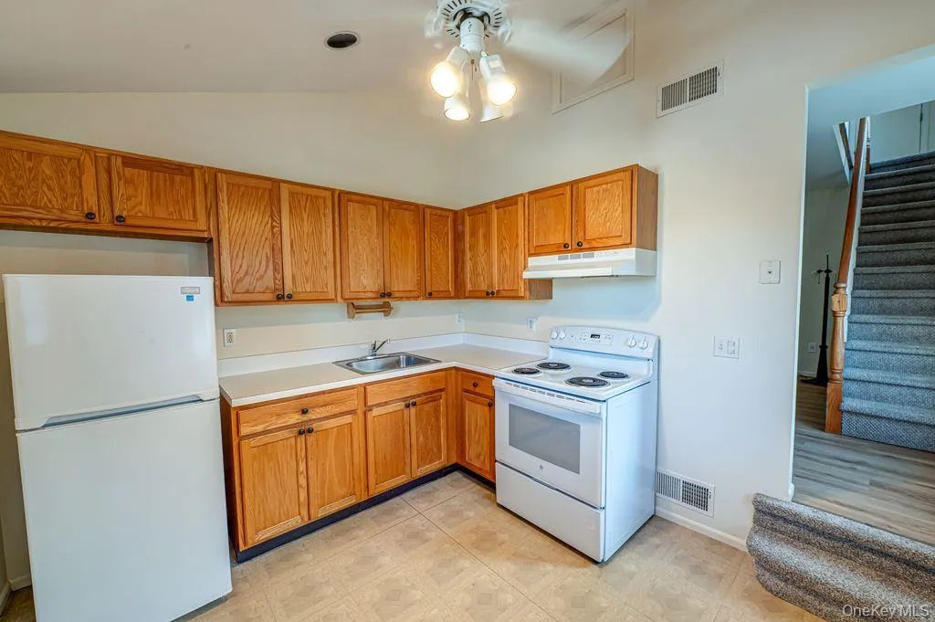 Kitchen with white appliances, light countertops, vaulted ceiling, under cabinet range hood, and brown cabinetry Kitchen with white appliances, light countertops, vaulted ceiling, under cabinet range hood, and brown cabinetry
