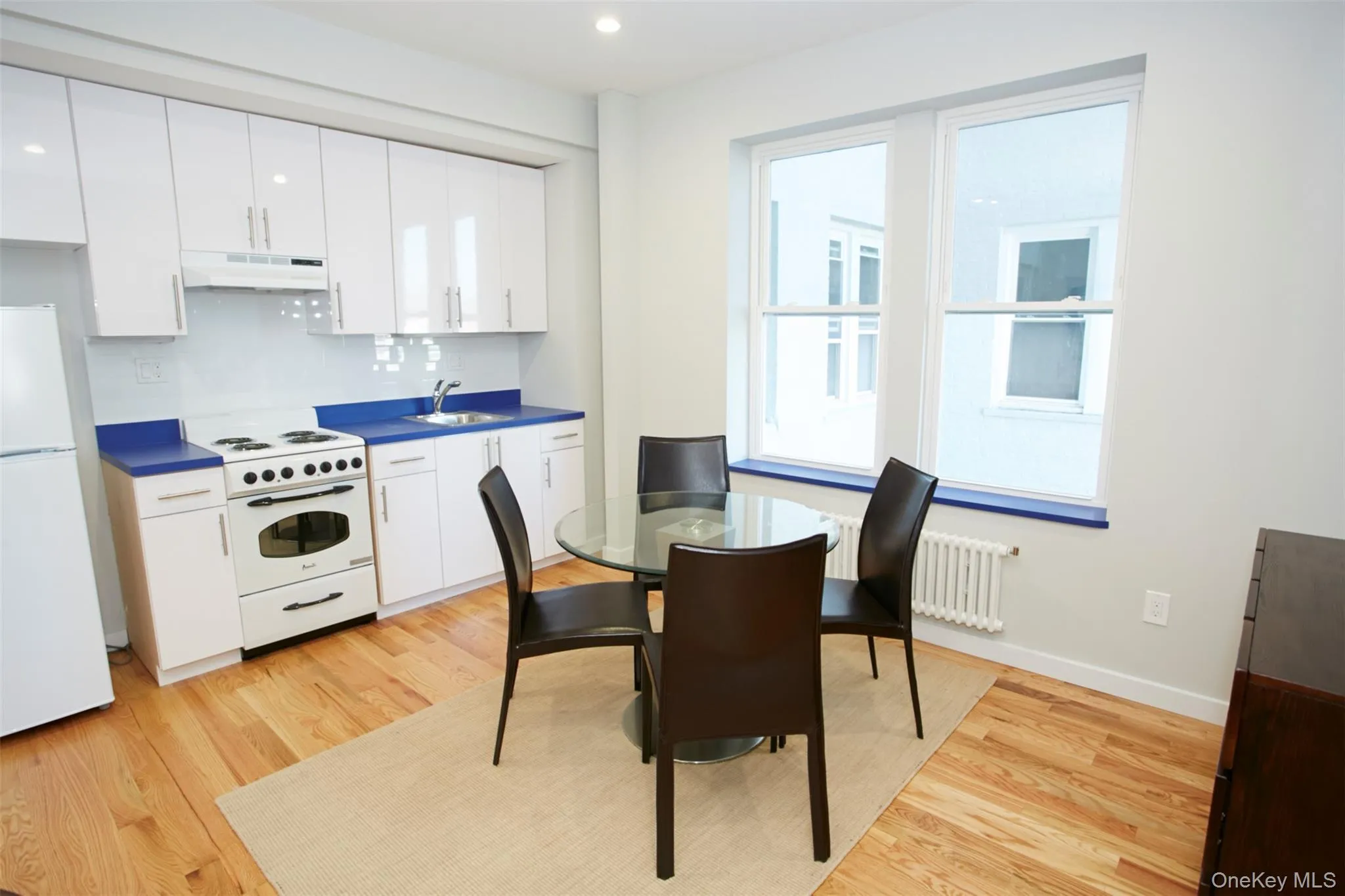 Kitchen with white appliances, white cabinetry, light wood-style flooring, and recessed lighting Kitchen with white appliances, white cabinetry, light wood-style flooring, and recessed lighting