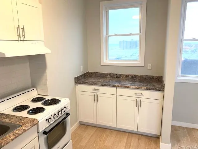 Kitchen with white range with electric cooktop, white cabinets, under cabinet range hood, light wood-type flooring, and dark stone countertops Kitchen with white range with electric cooktop, white cabinets, under cabinet range hood, light wood-type flooring, and dark stone countertops