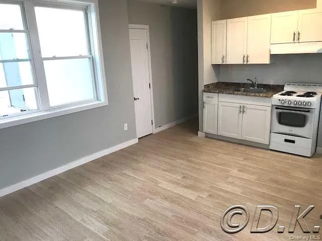Kitchen featuring white range oven, white cabinets, light wood finished floors, under cabinet range hood, and dark stone counters Kitchen featuring white range oven, white cabinets, light wood finished floors, under cabinet range hood, and dark stone counters